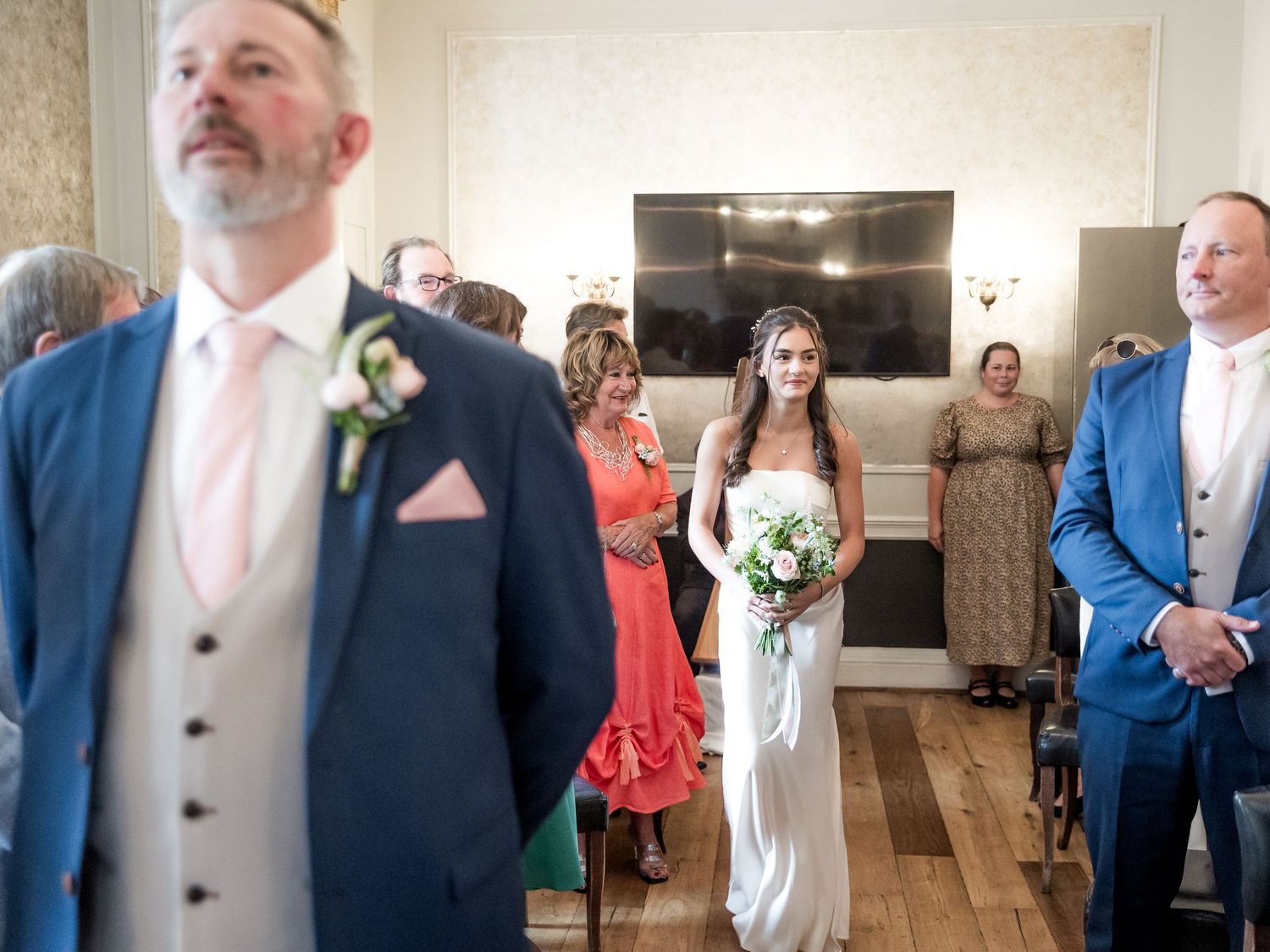 Wedding ceremony entrance in an elegant room with guests watching and a couple in formal attire.