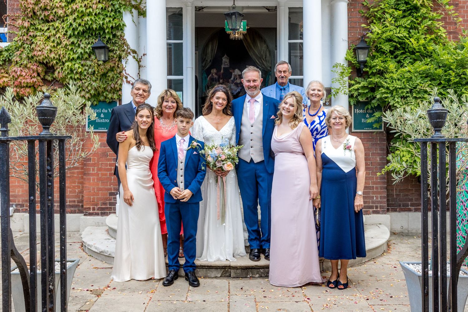 Wedding group photo taken outside a traditional brick building entrance.
