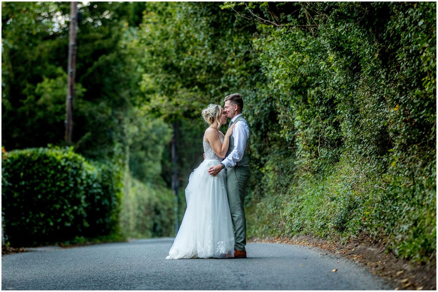 Wedding couple poses for portraits along lush green garden pathway.
