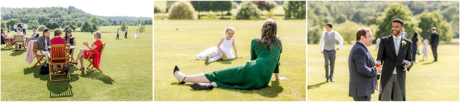 Wedding guests relaxing on red chairs and blankets on a sunny lawn during an outdoor celebration.