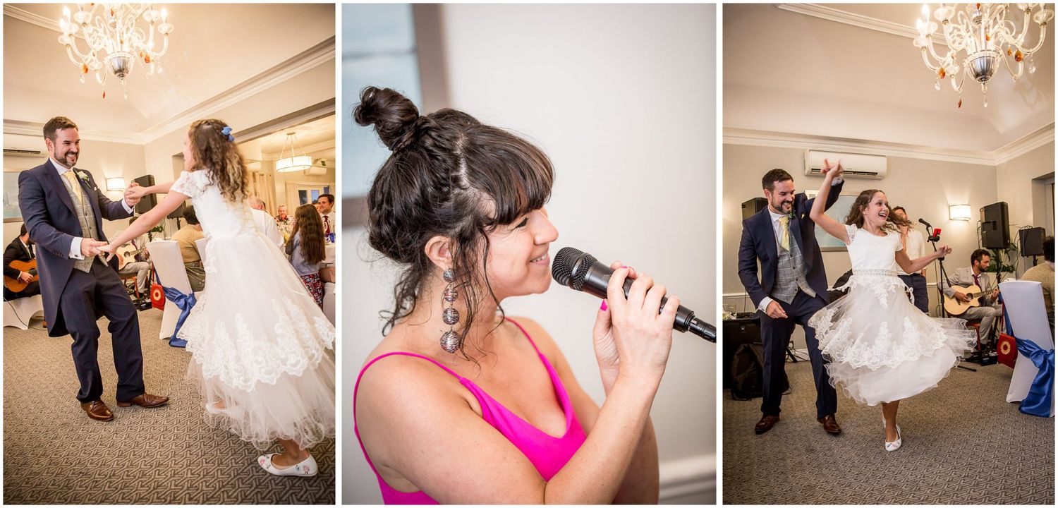 Wedding guests dance and celebrate on a wooden dance floor under elegant crystal chandeliers at an indoor reception.