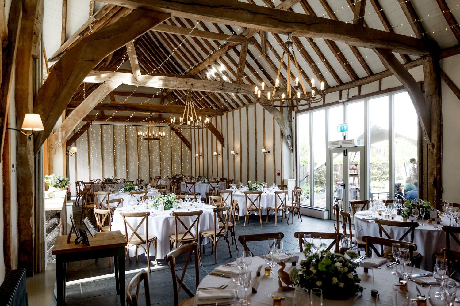 Interior view of a grand barn wedding venue with exposed wooden beams and elegant table settings.