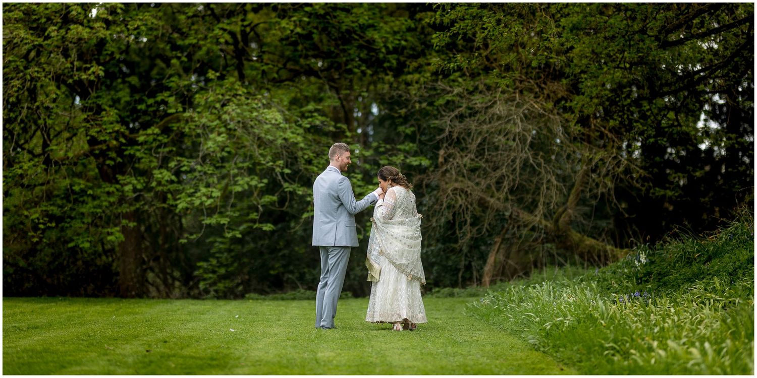 Couple walking hand in hand through a green spring meadow during their wedding photoshoot.