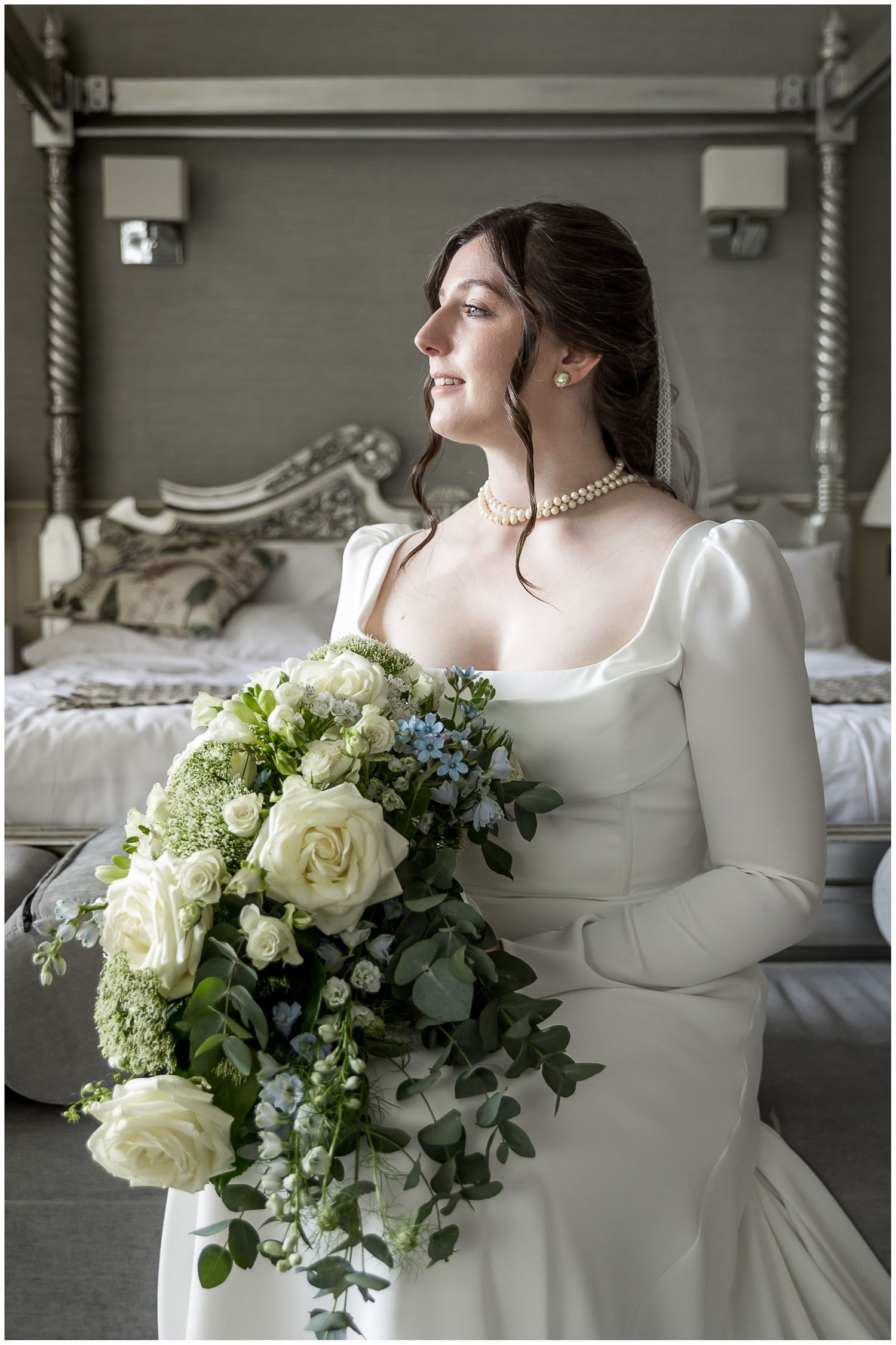Elegant bridal portrait with white roses and greenery bouquet on ornate bed.