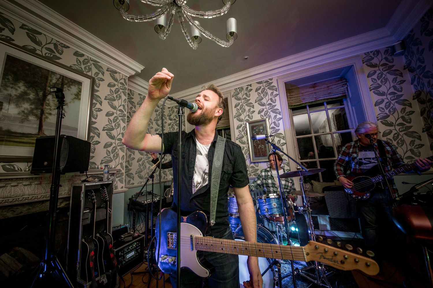 A musician performs energetically with a guitar under chandelier lighting.