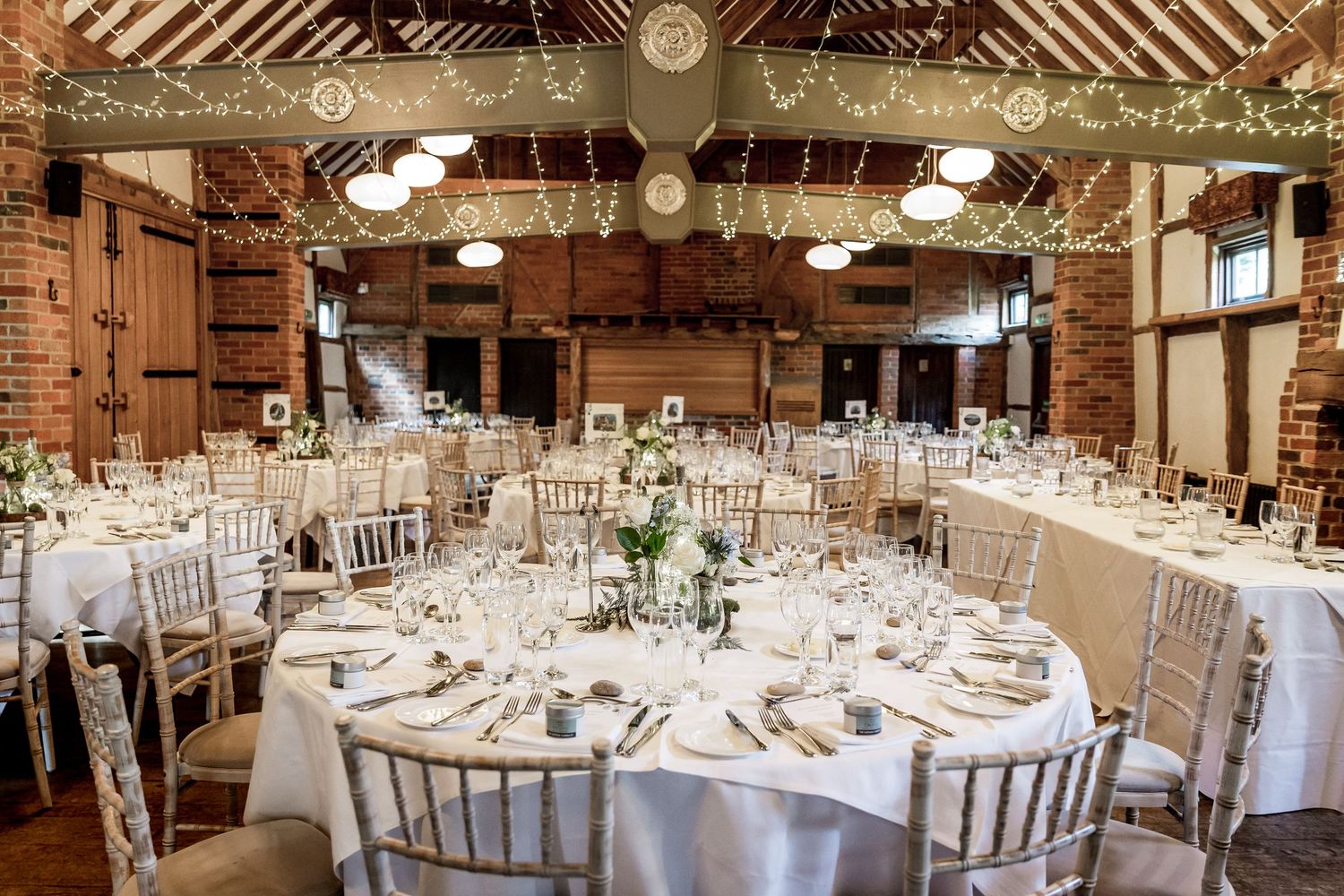 Elegant wedding reception setup in a rustic barn venue with white tablecloths and wooden beams.