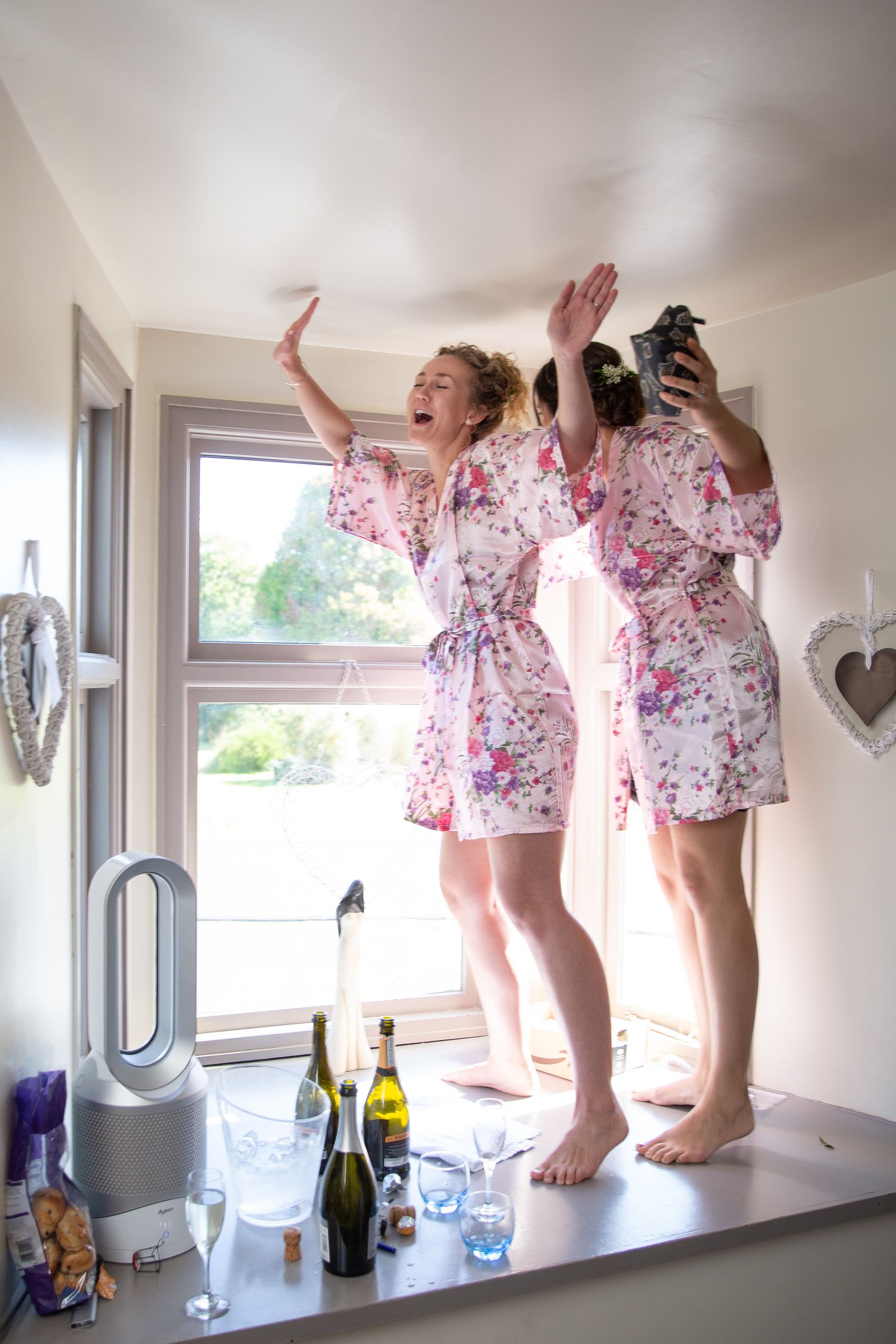 Two people in floral robes celebrating with champagne by a window.