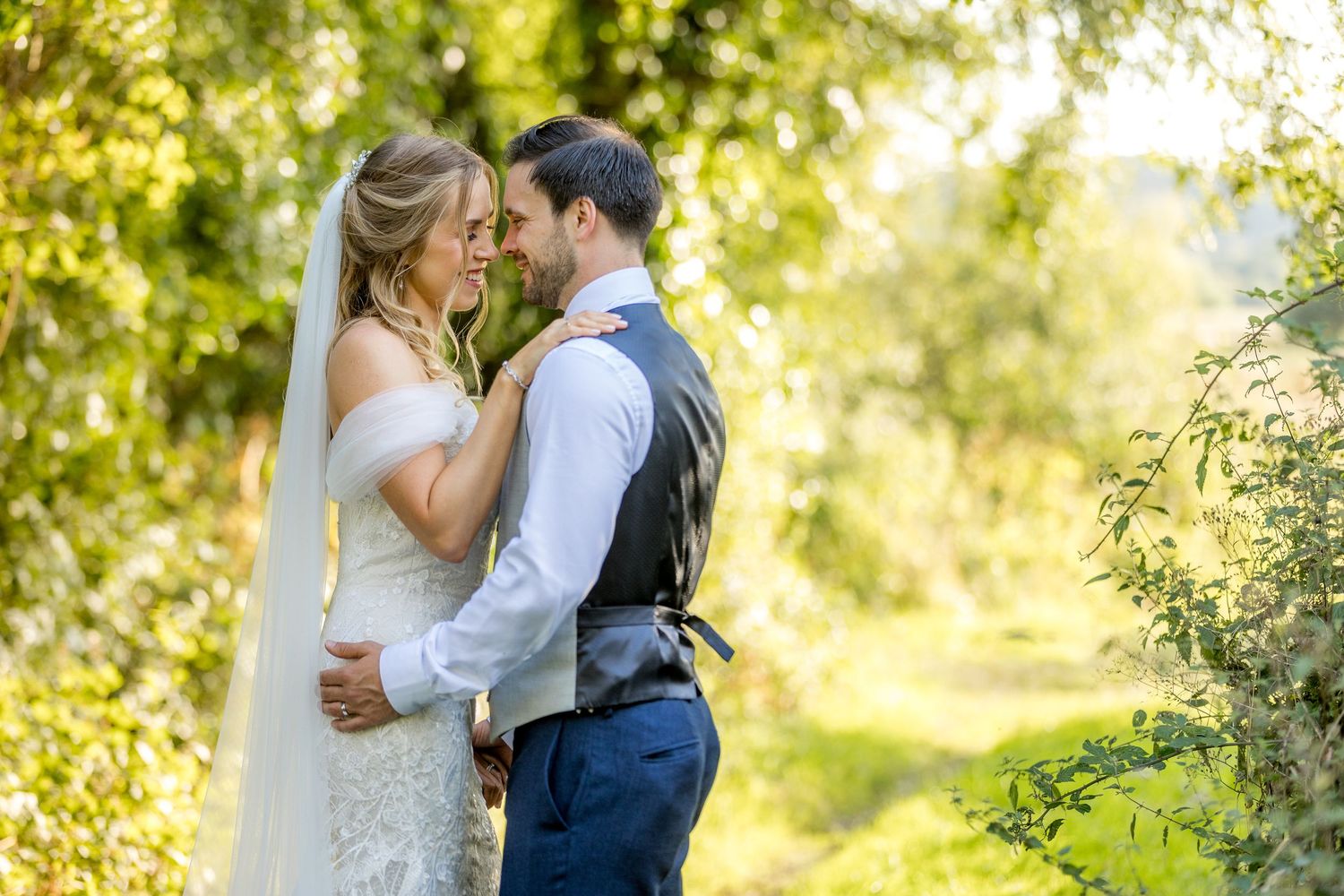 Wedding couple embracing in a sunlit garden setting with lush greenery.
