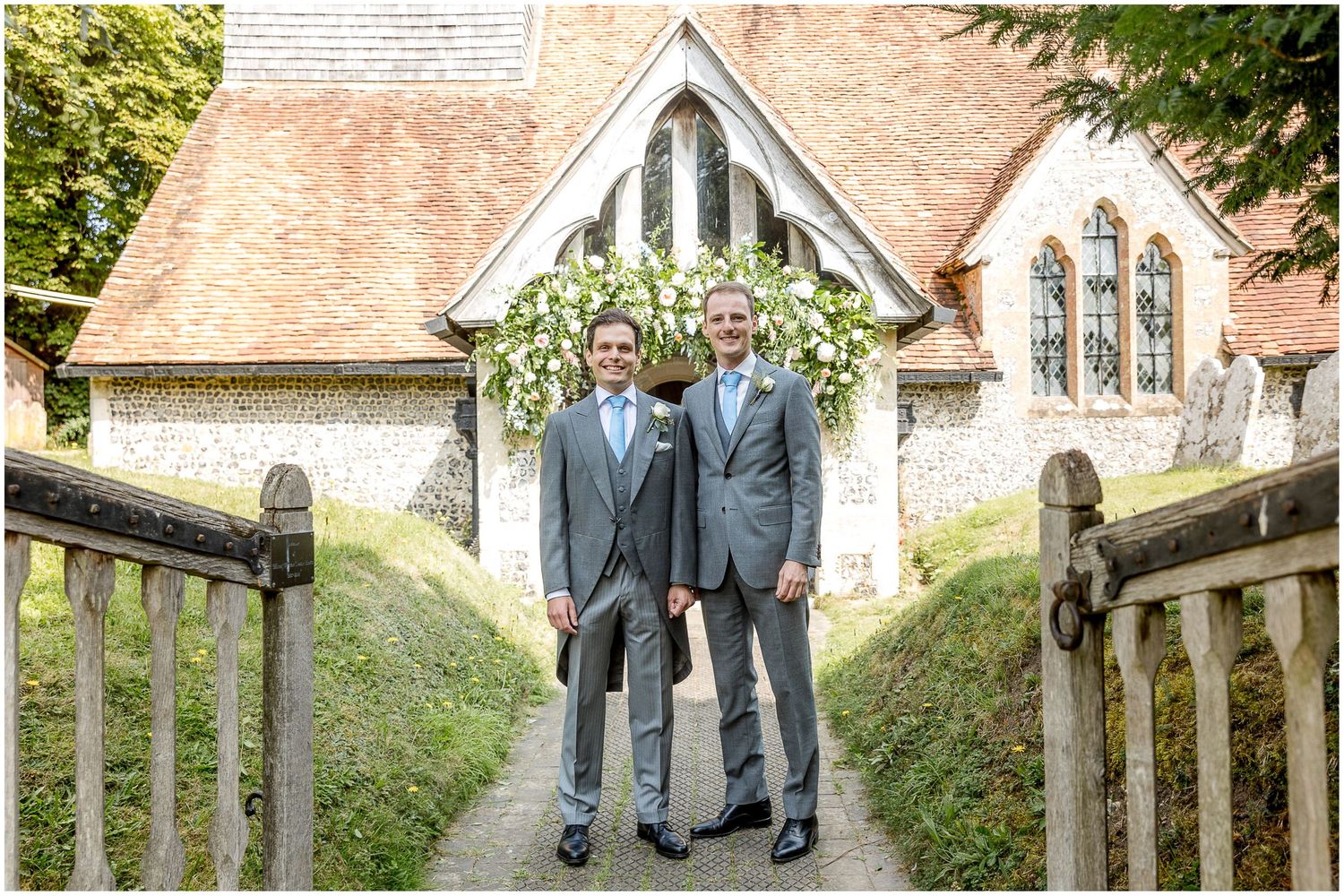 Wedding party walking along stone pathway outside historic brick church with beautiful landscaping.