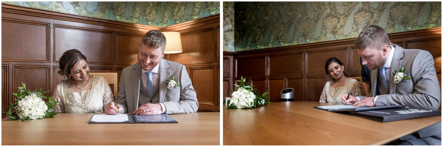 Couple signing marriage documents at a wooden table in an elegant indoor setting.
