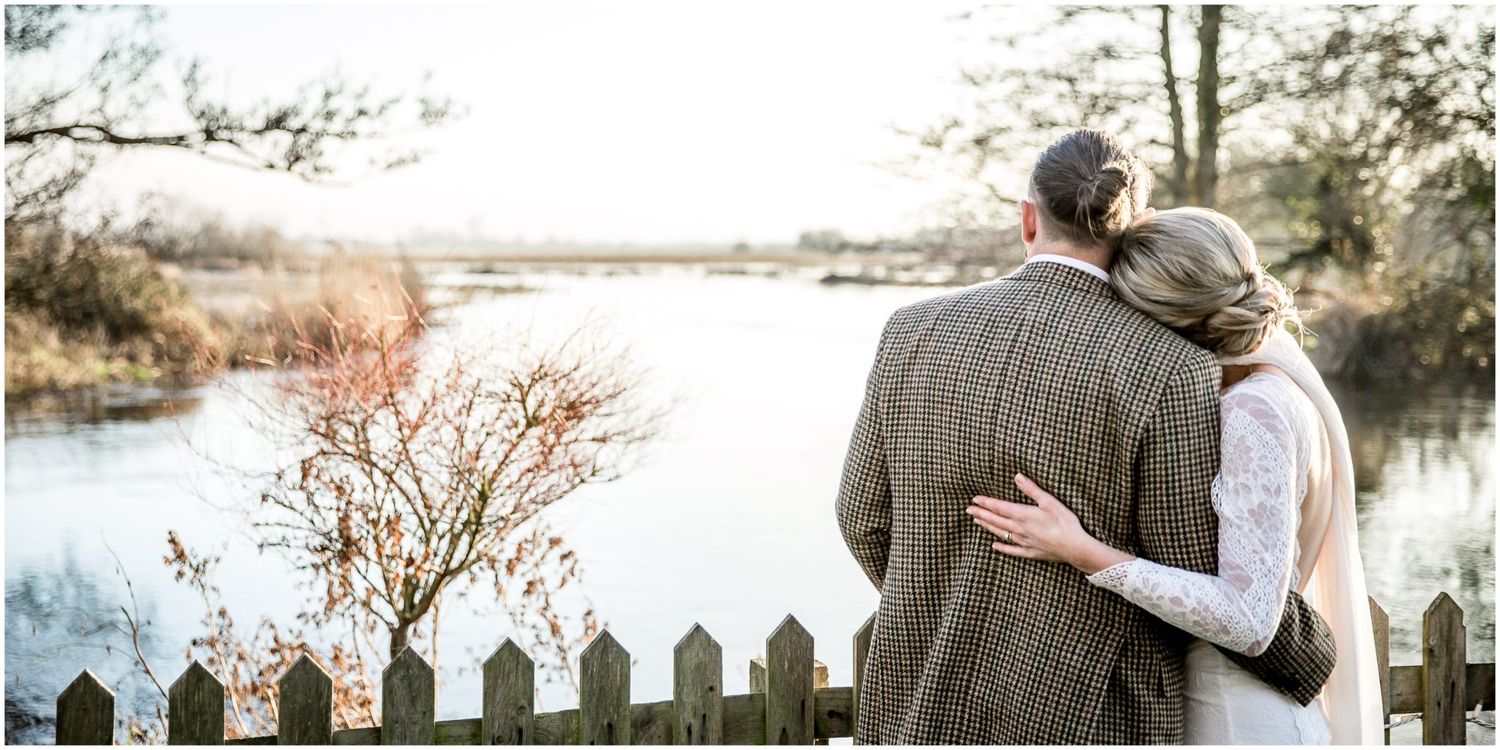 Romantic winter wedding portraits with picket fence and flooded landscape backdrop.