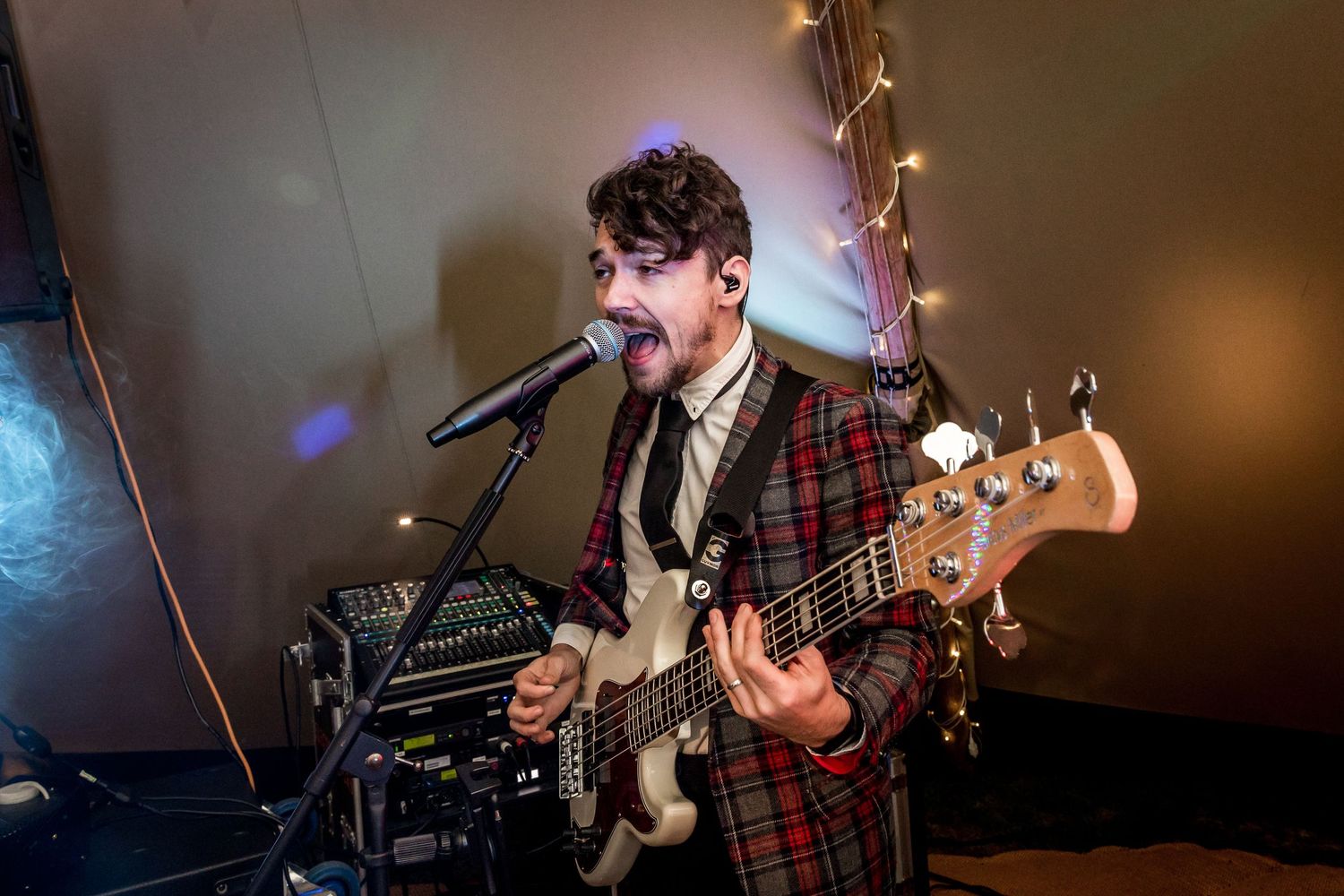 A musician in plaid plays bass guitar and sings during a wedding reception performance.