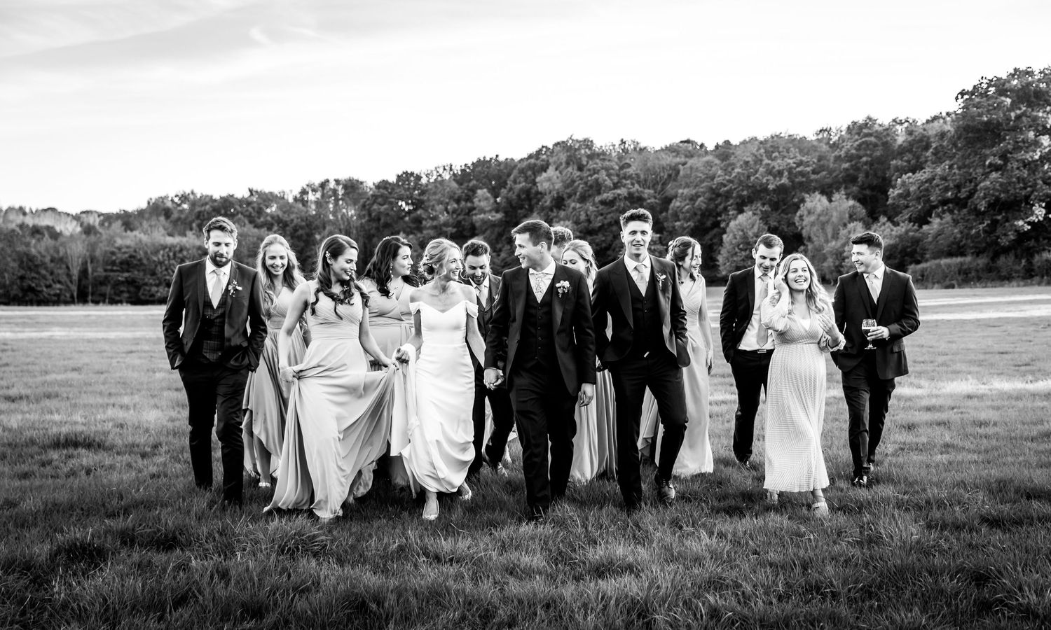 Black and white panoramic shots of wedding party posing outdoors on grassy lawn.