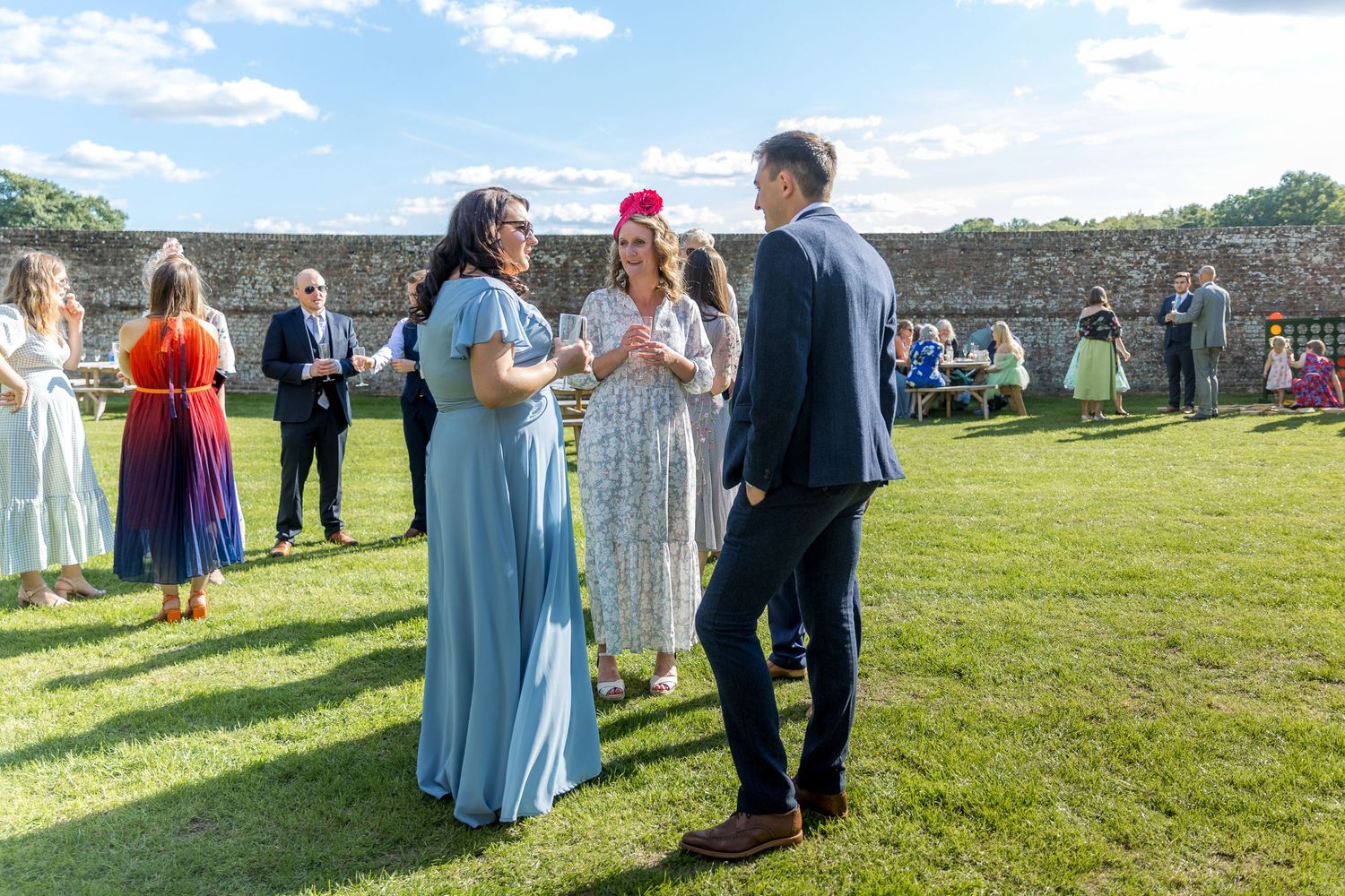 Wedding guests gather on a grassy lawn under blue skies at an outdoor venue.