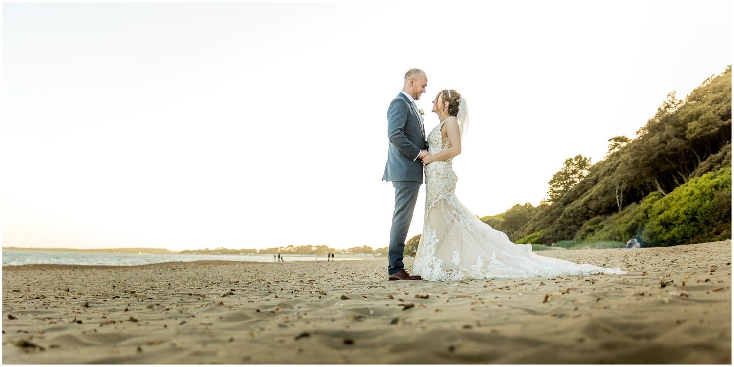 Wedding couple poses for romantic photos on a beach with cliffs in the background.