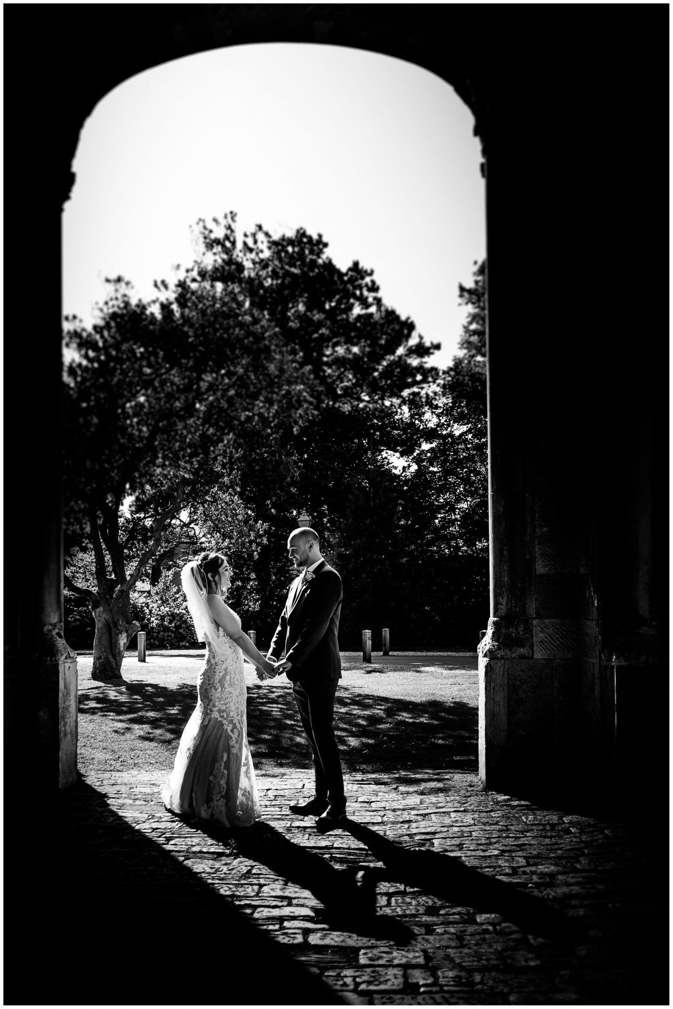 Dramatic black and white silhouettes of a wedding couple through stone archways.