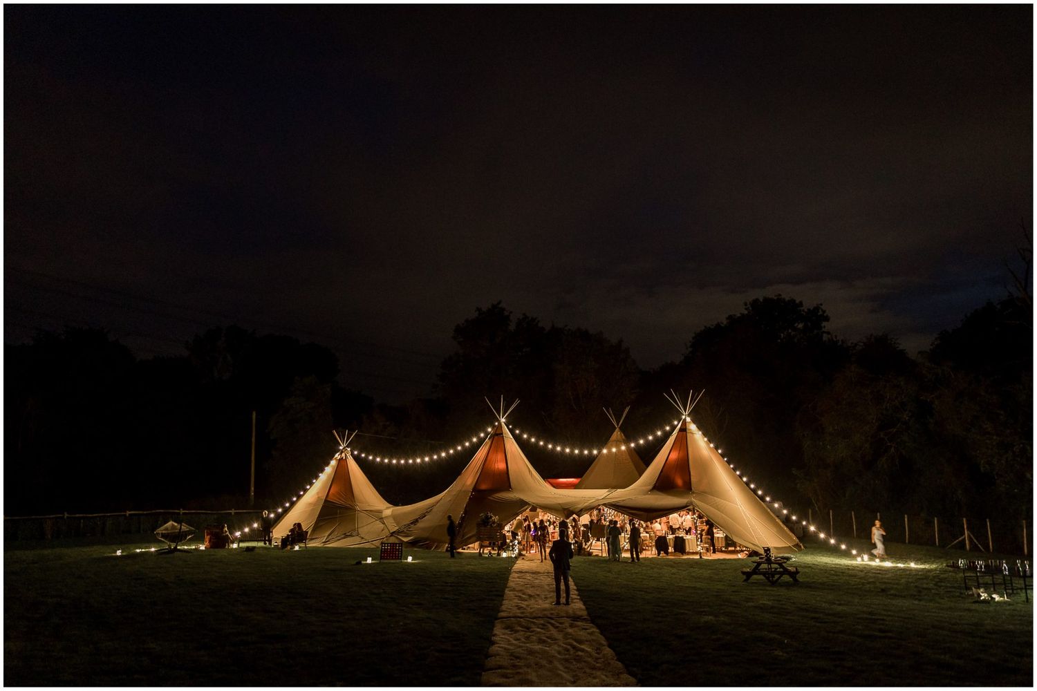 Illuminated wedding tent glowing at night with string lights creating a magical atmosphere.