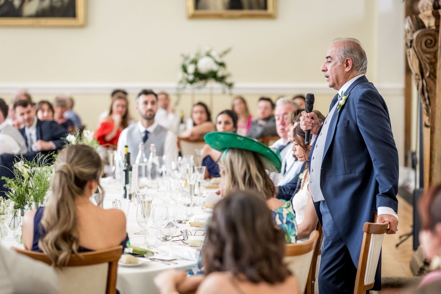 Formal wedding reception with guests seated at decorated tables listening to speeches.