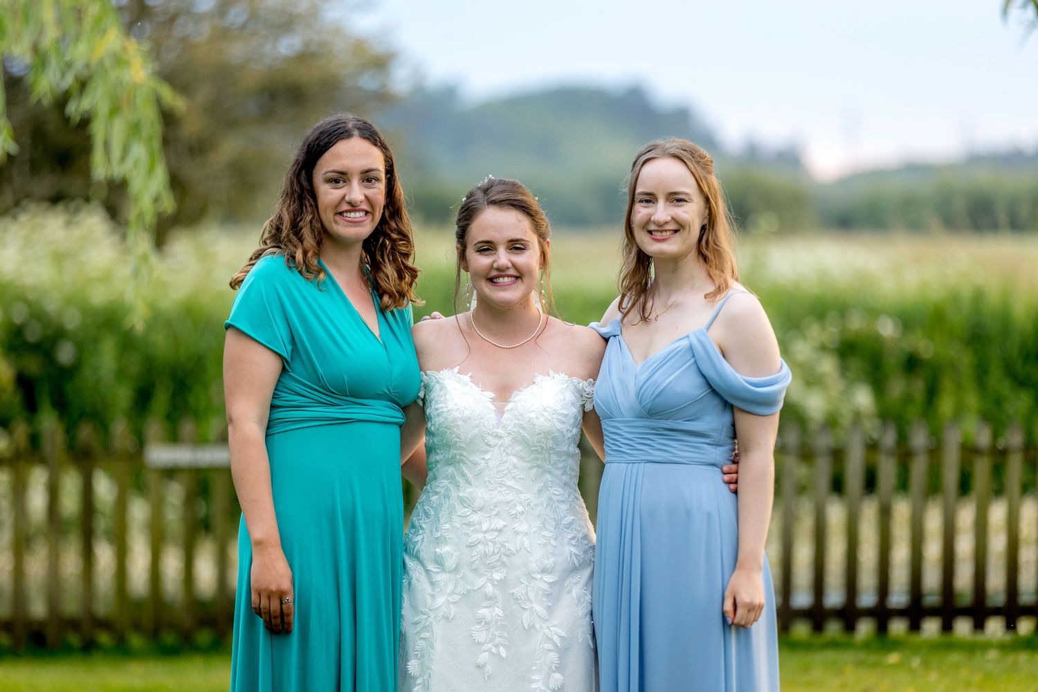 Wedding party members in teal and light blue dresses pose together on grassy grounds.