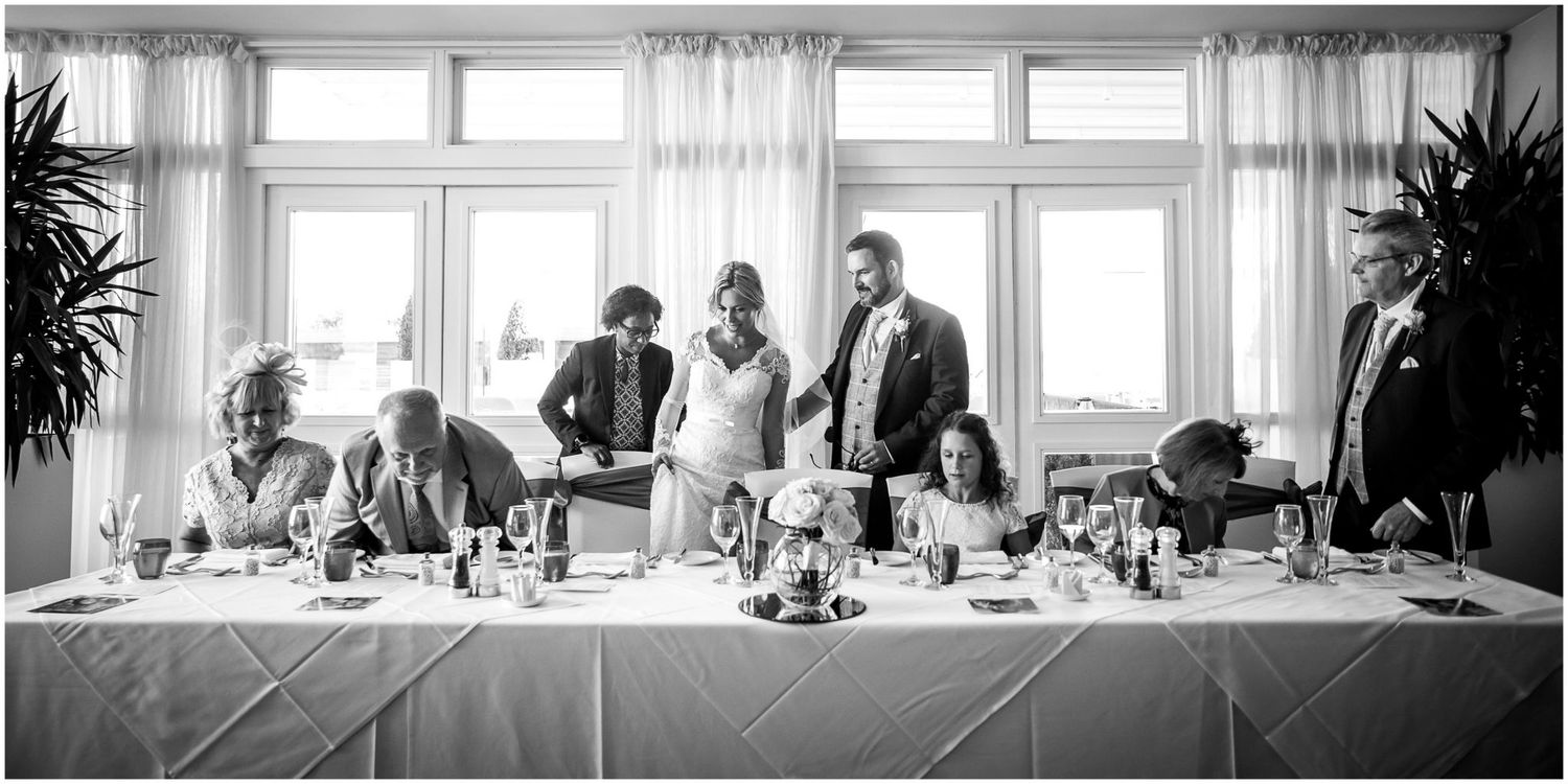 A black and white photo of a formal dining table setup with guests gathered around during a celebration event.