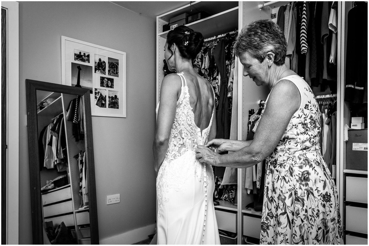 The bride's mother helps the bride into her wedding dress