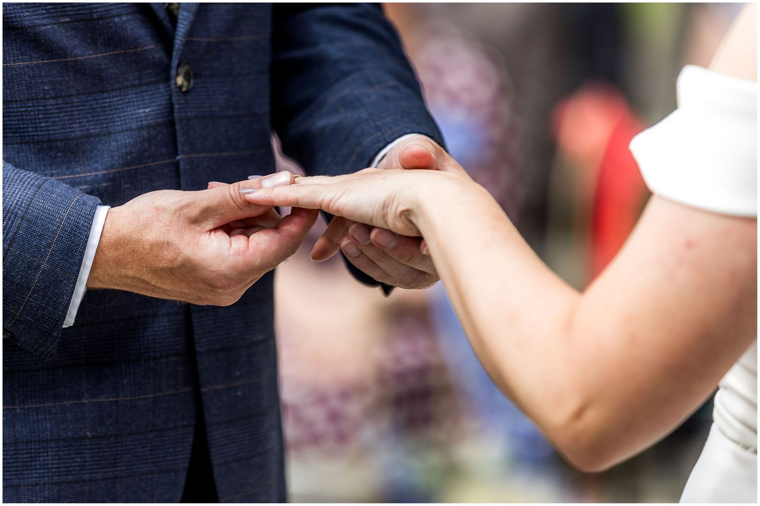 Groom placing a wedding ring on bride's finger during a Dorset outdoor wedding ceremony.