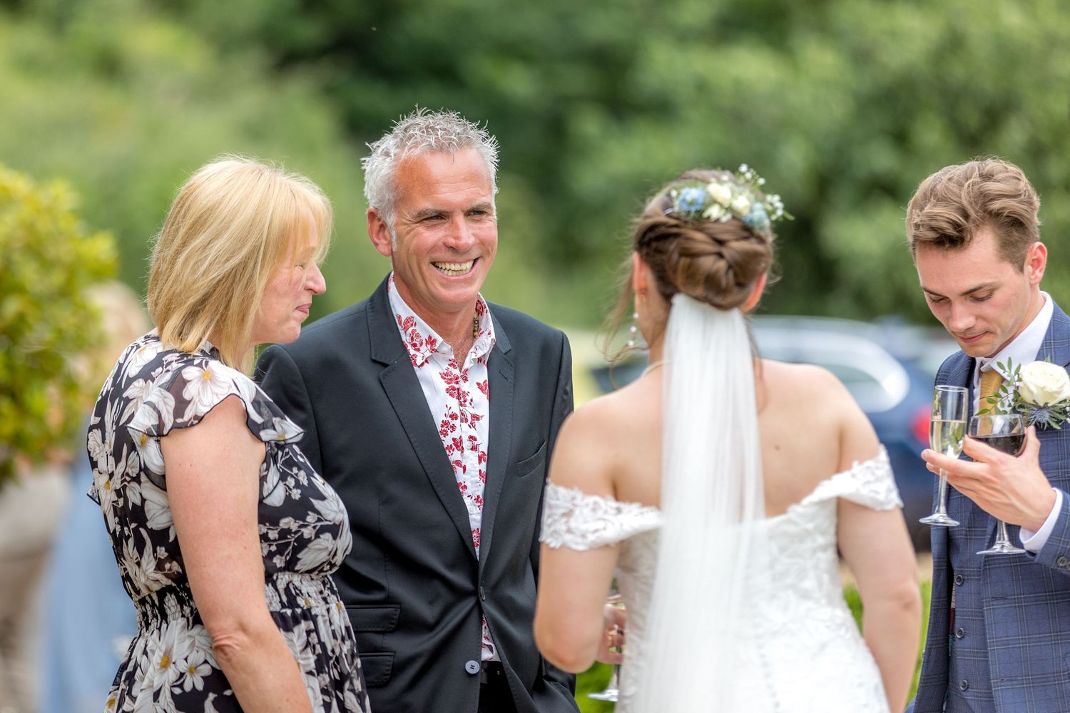 Wedding party and guests mingling outdoors on sunny garden lawn.