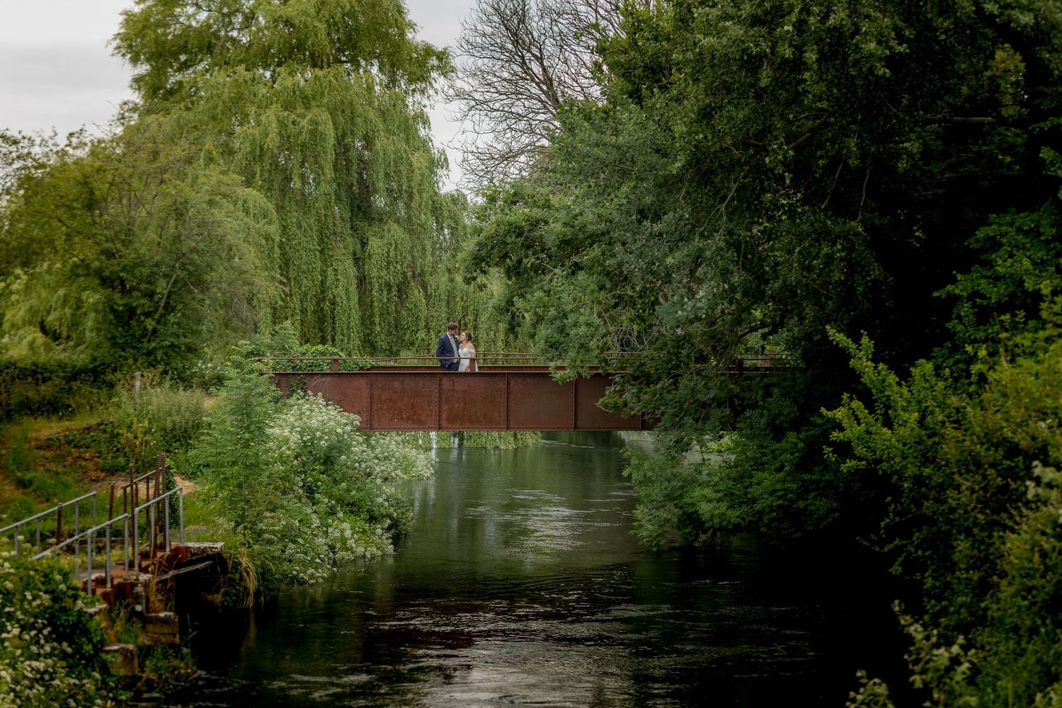 Scenic garden pathway with pond and willow trees creates peaceful wedding backdrop.