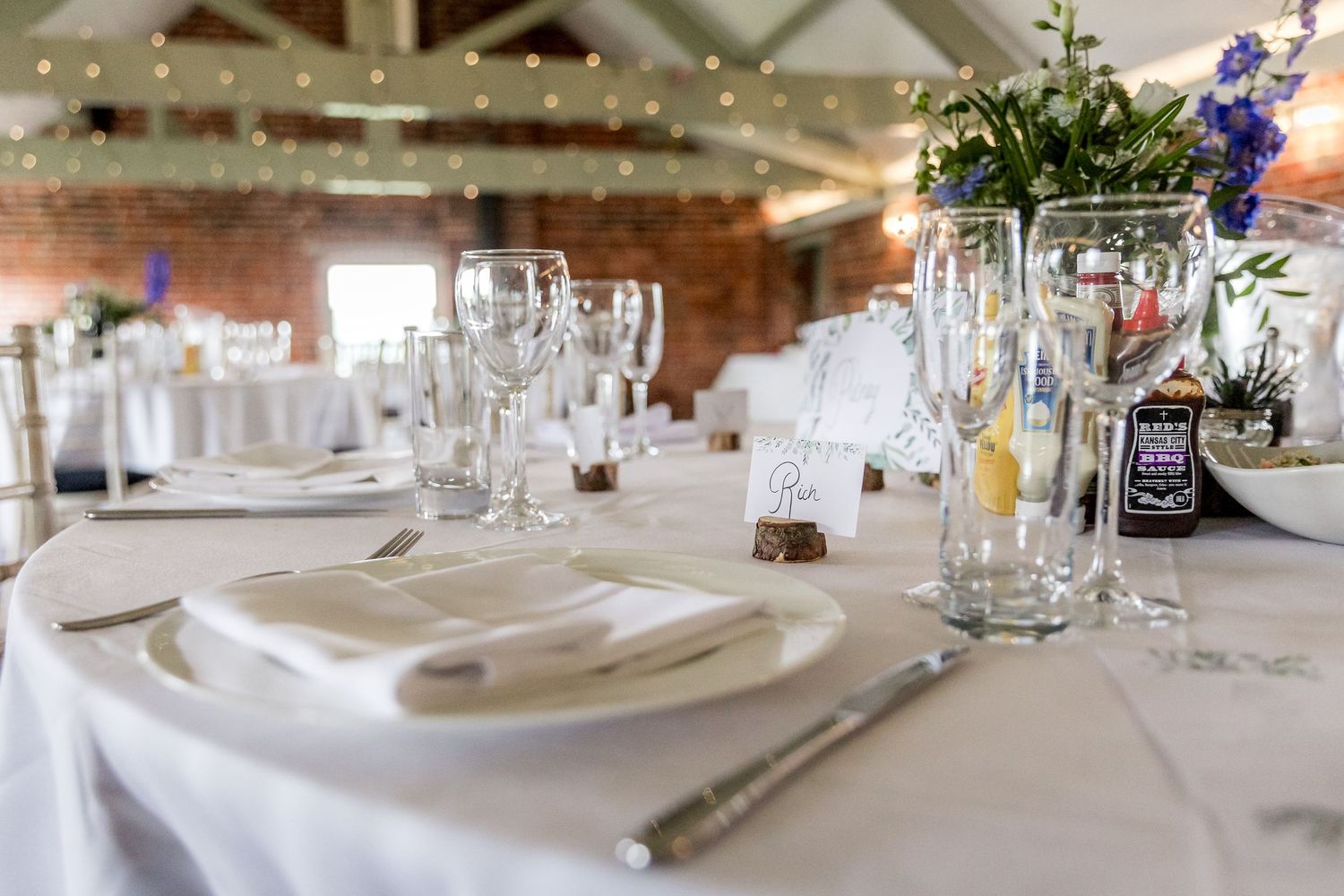 Wedding reception tables decorated with blue flowers and glassware in industrial brick space.