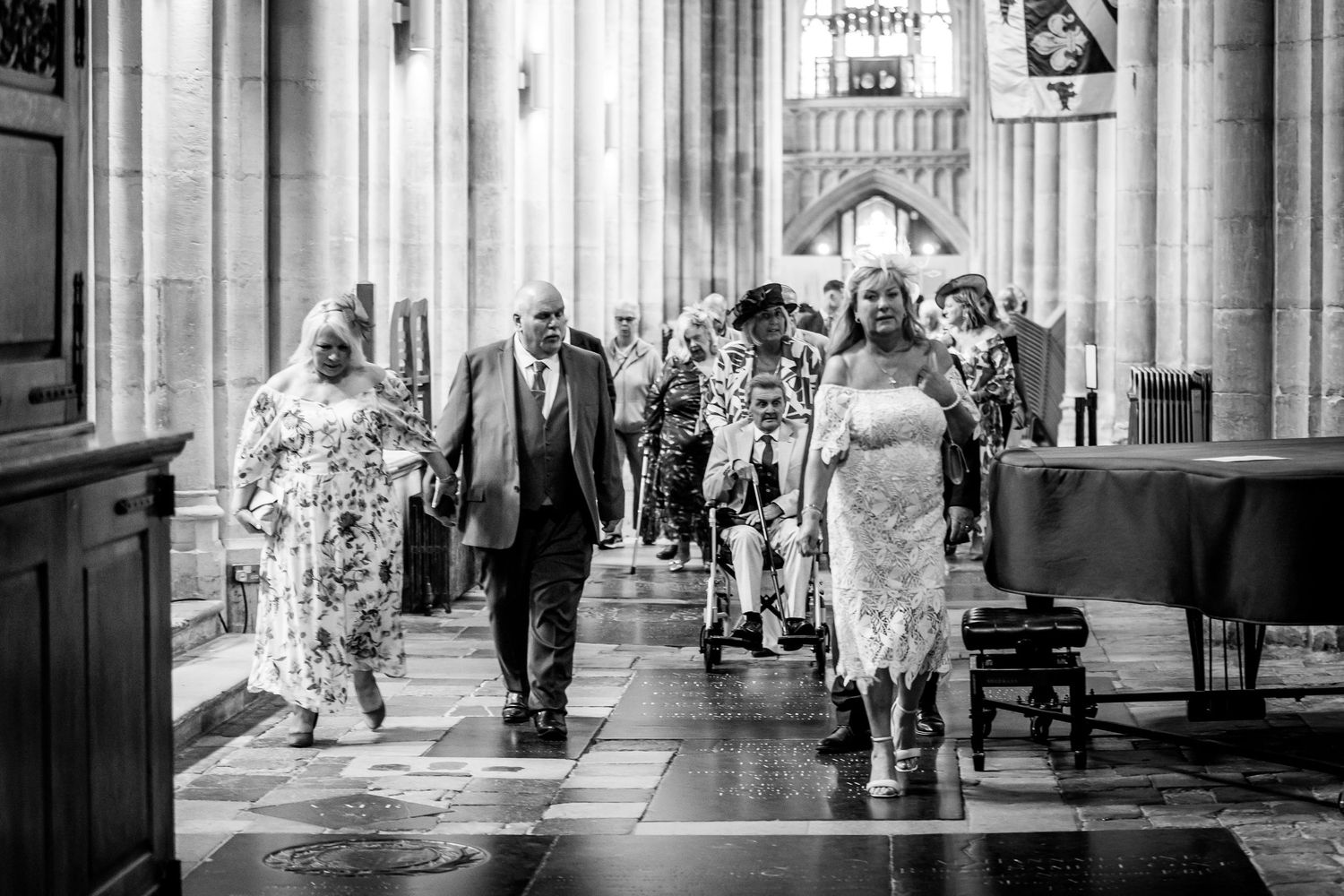 Black and white photograph of people walking through a grand cathedral corridor.