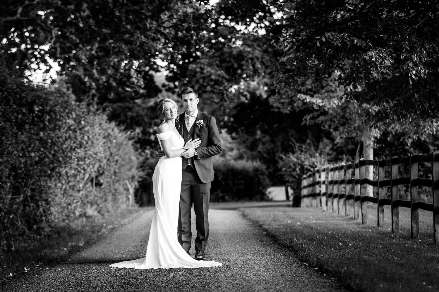 Artistic black and white wedding photos showing a couple walking through a tree-lined path.