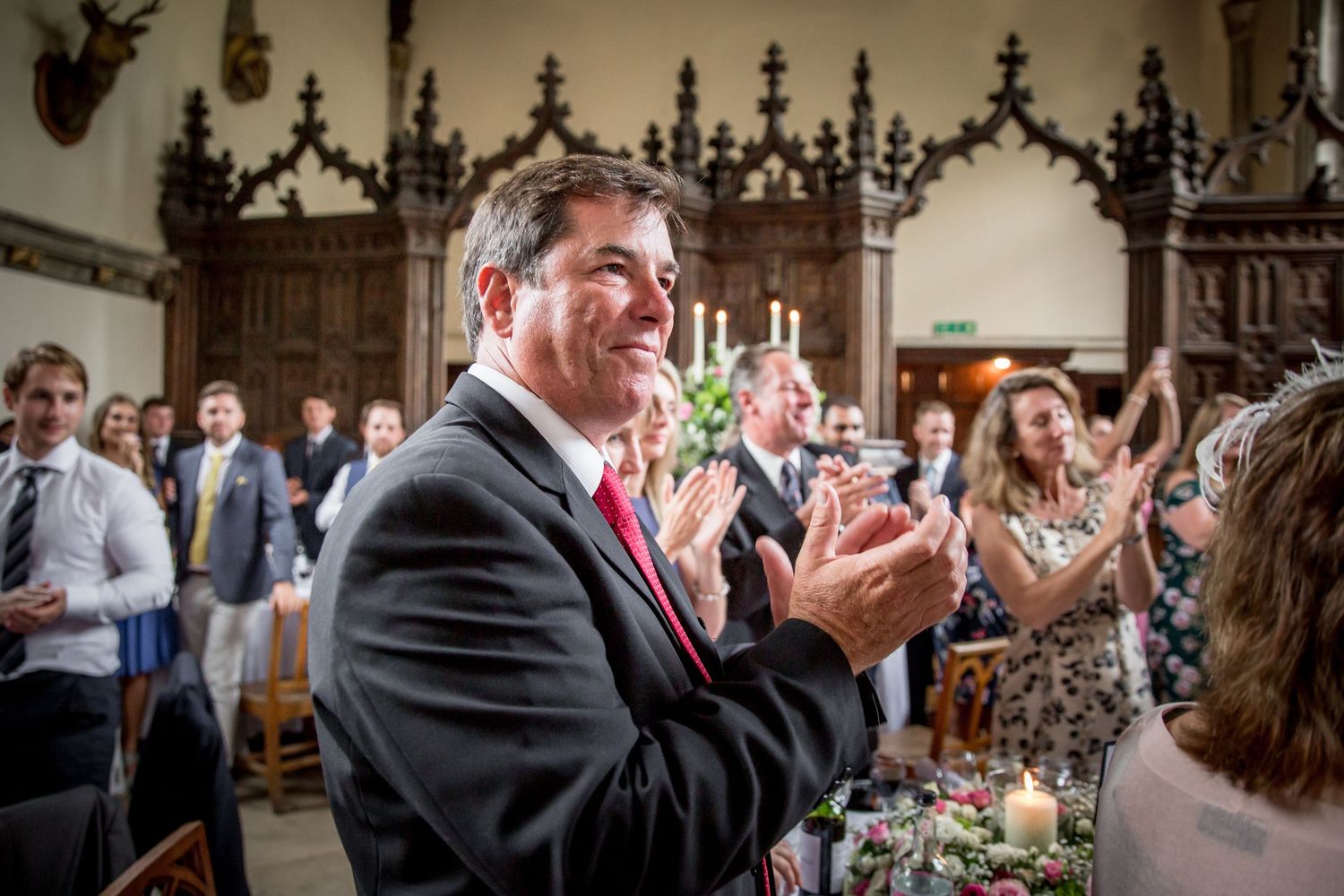 Wedding guests celebrate during an indoor reception with joyful expressions and raised hands.