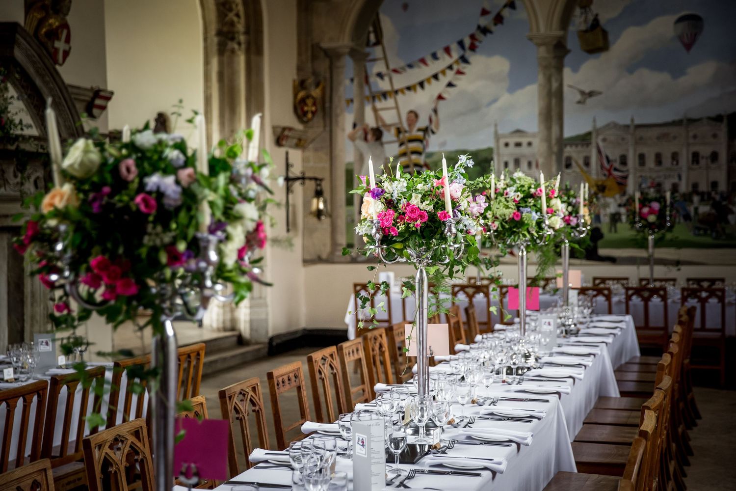 Grand dining hall decorated with floral arrangements and place settings for an elegant wedding reception.