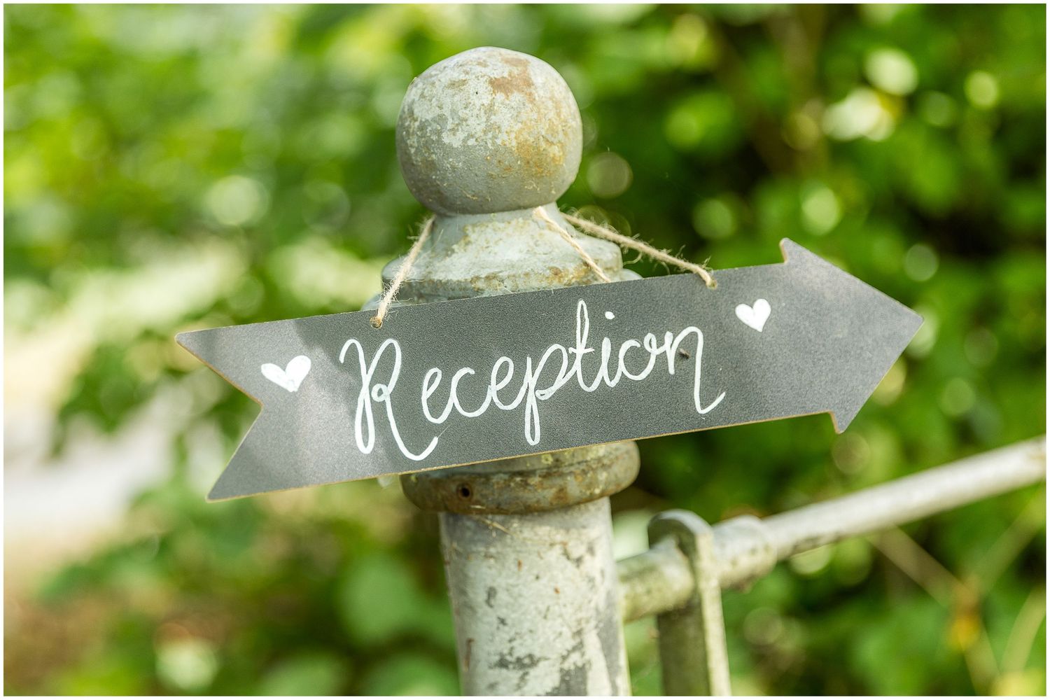 Rustic wooden directional signs for wedding reception with green foliage background.