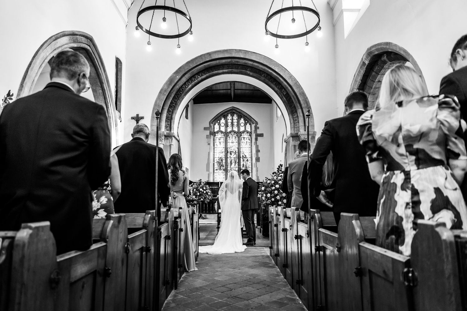 Interior view of a church with circular chandeliers and gothic arches during a wedding ceremony.