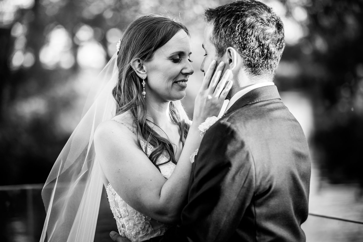 A tender black and white wedding moment captured between newlyweds sharing an intimate embrace outdoors.