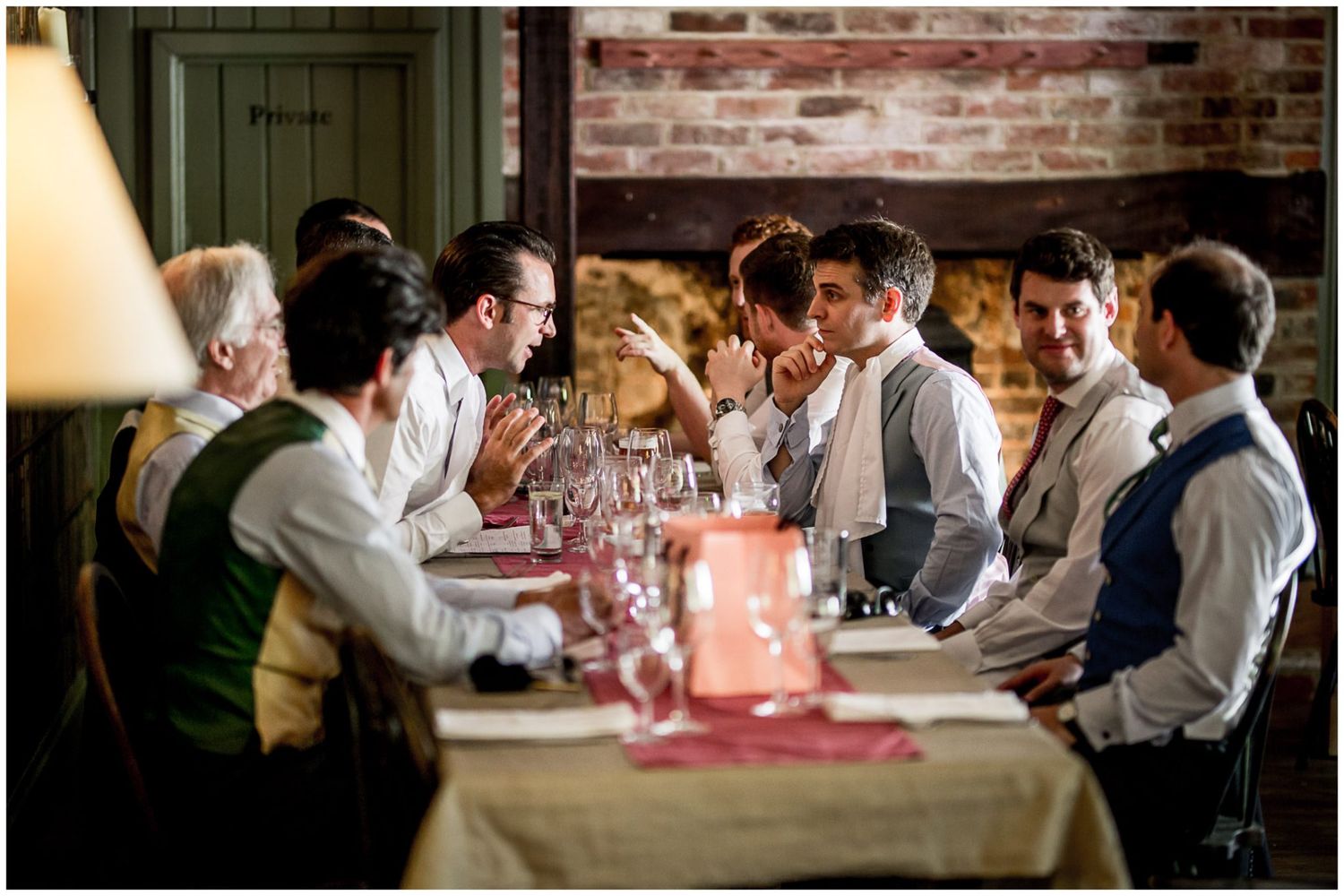 Wedding guests enjoy dinner and conversation at rustic venue with exposed brick walls and wooden beams.