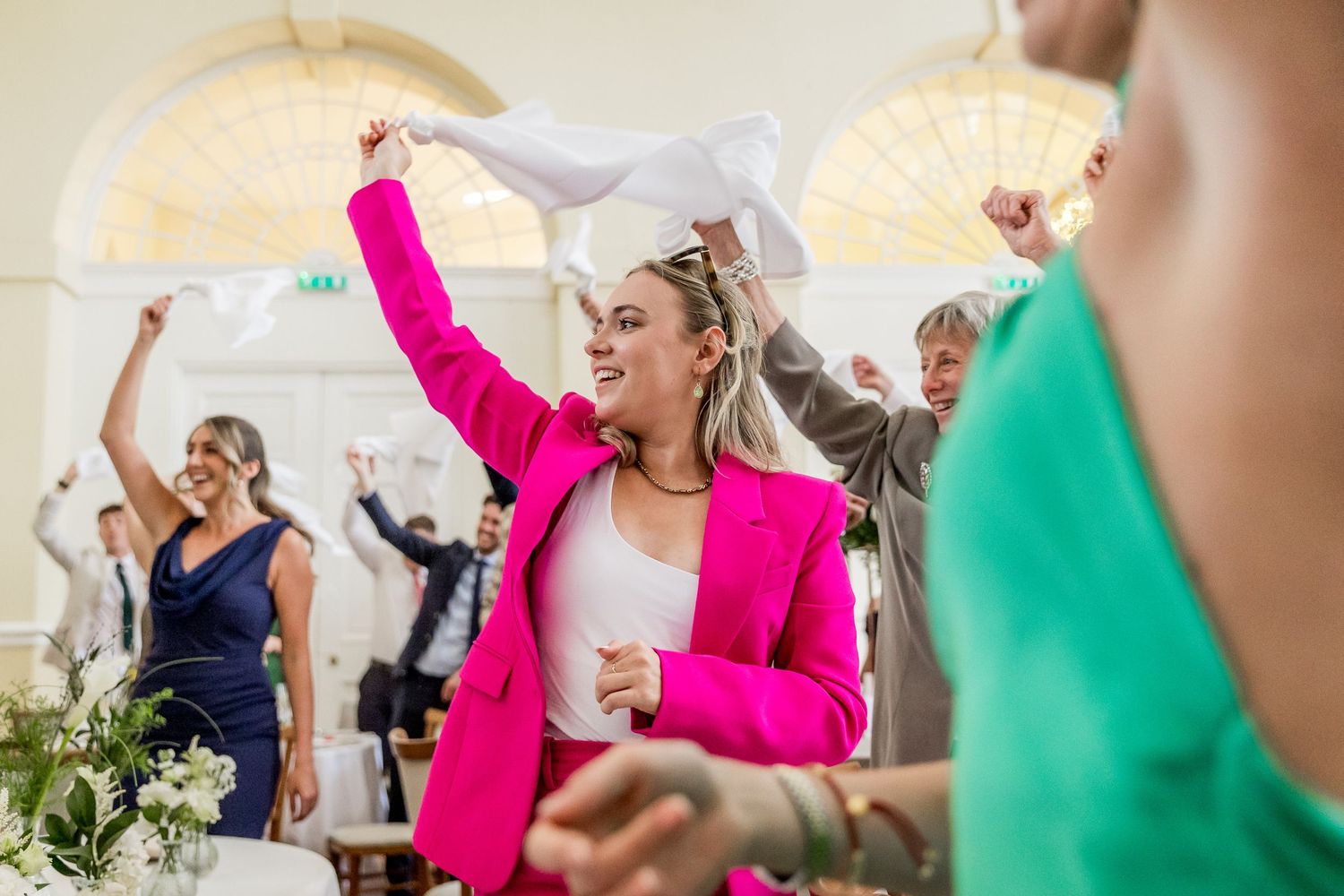 Wedding party dancing and celebrating in a bright reception hall with colorful attire.
