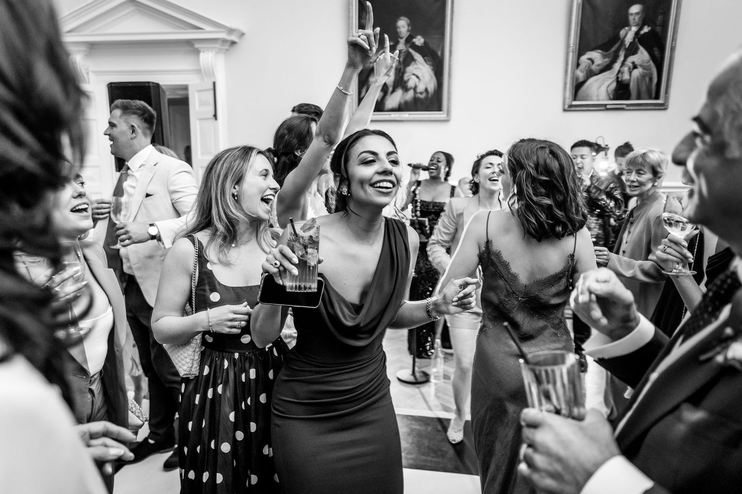 Wedding guests dancing and socializing in a formal venue with portrait paintings on the walls.
