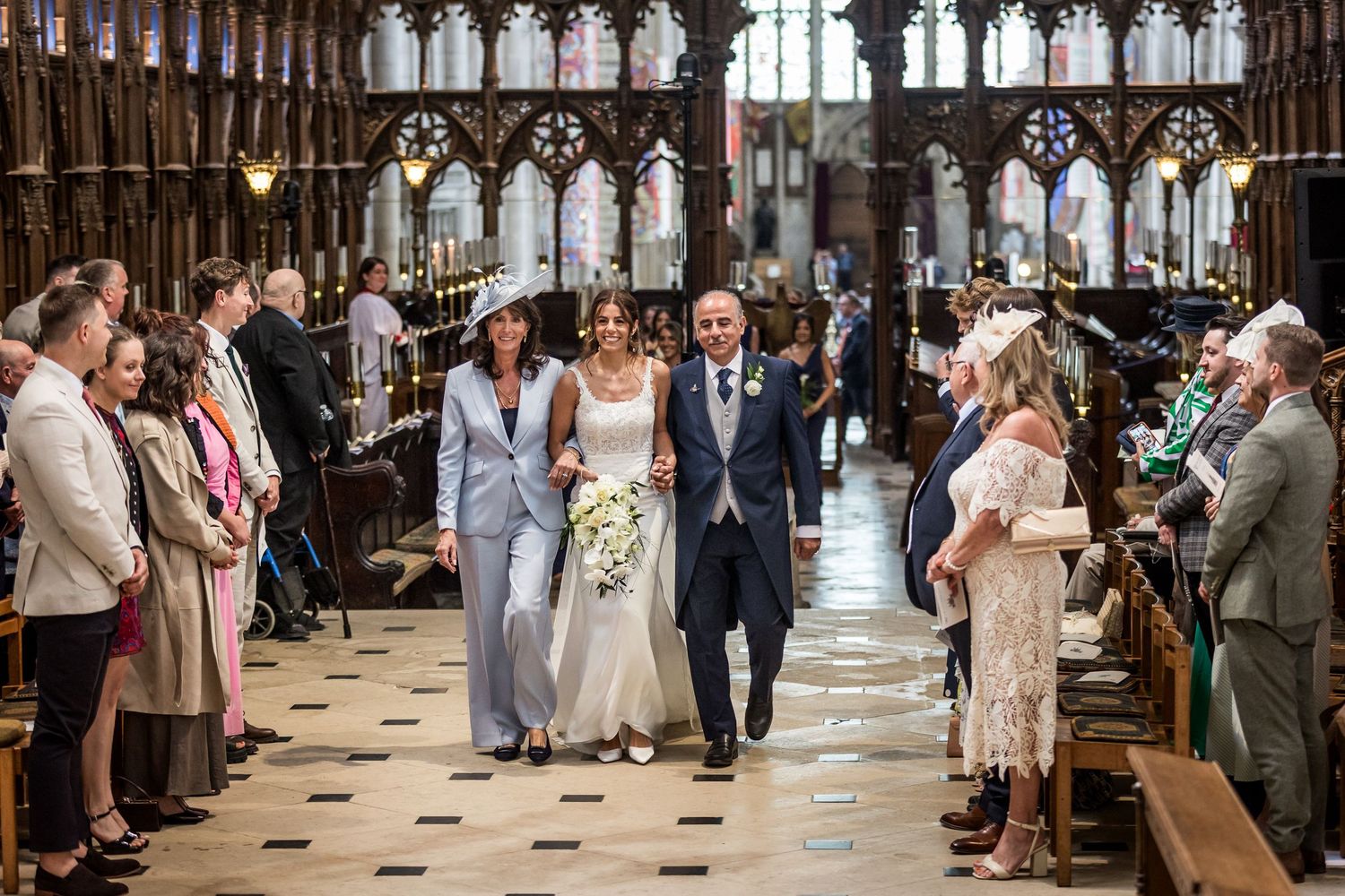 Wedding procession moves through a grand cathedral aisle lined with elegant Gothic archways.
