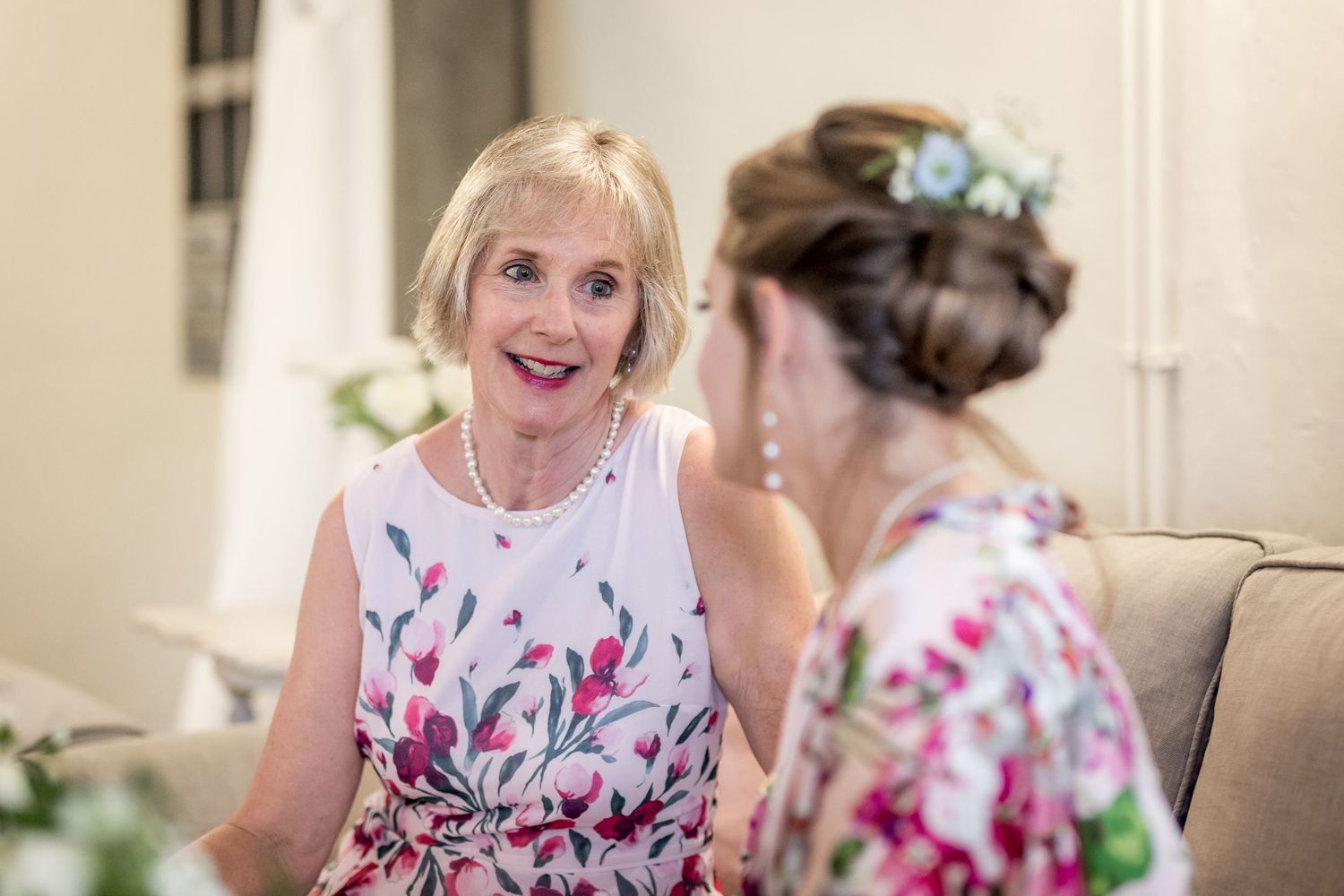 Women in colorful floral dresses smile and chat during an elegant event.