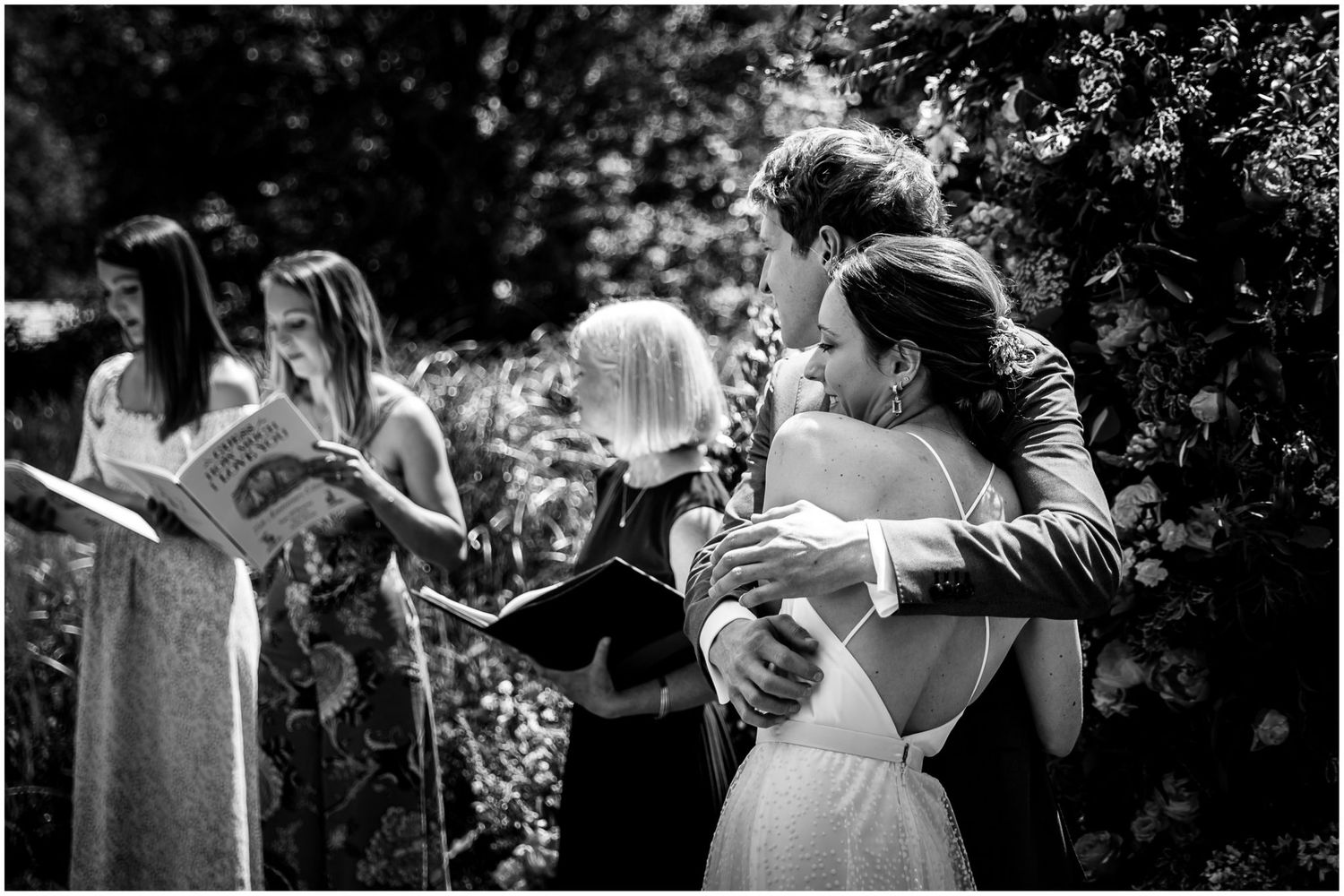 Couple shares intimate moment during outdoor garden wedding ceremony surrounded by lush greenery.