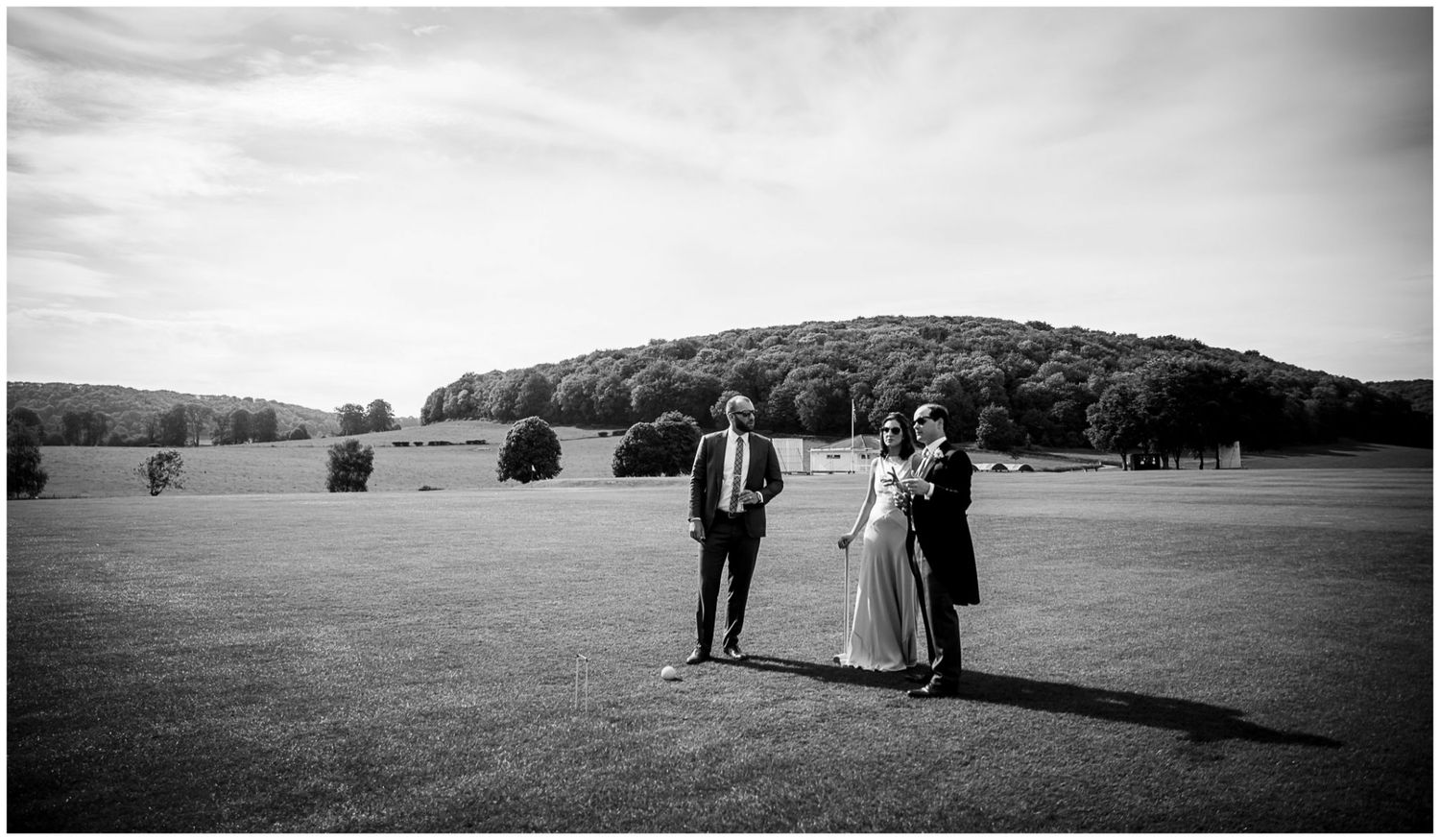 A black and white panoramic view of people walking across a vast grassy field with trees in the distance.