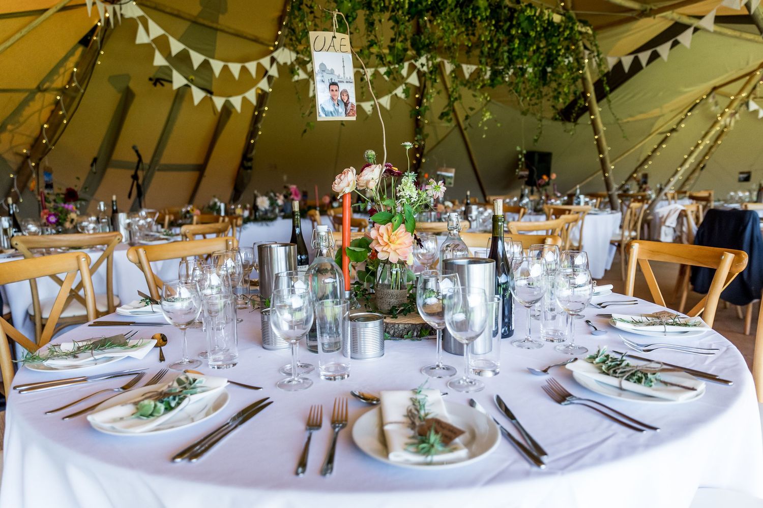 Elegant table settings with white linens and floral centerpieces under tent lighting.