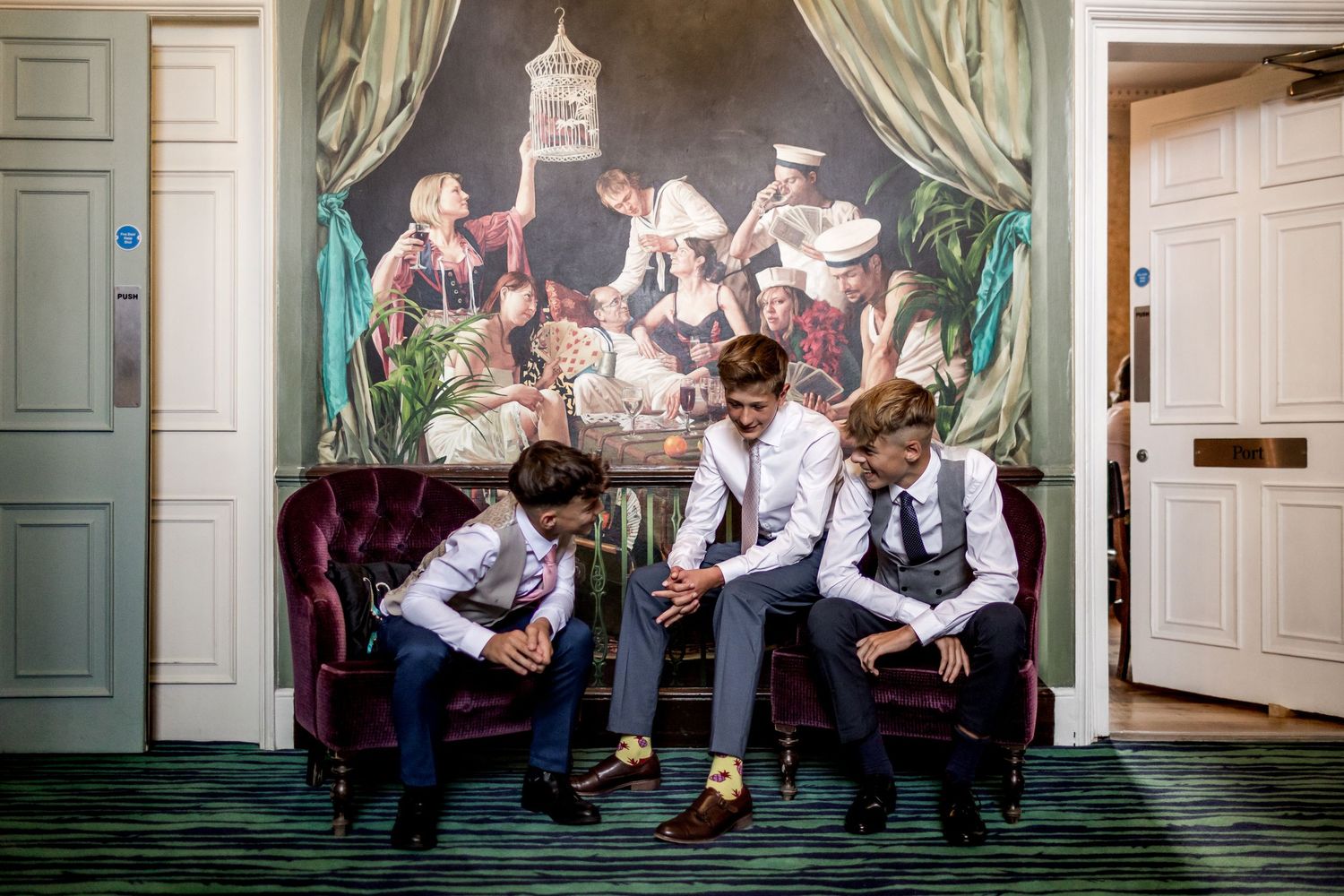Wedding party members relaxing against ornate wall with green curtains.