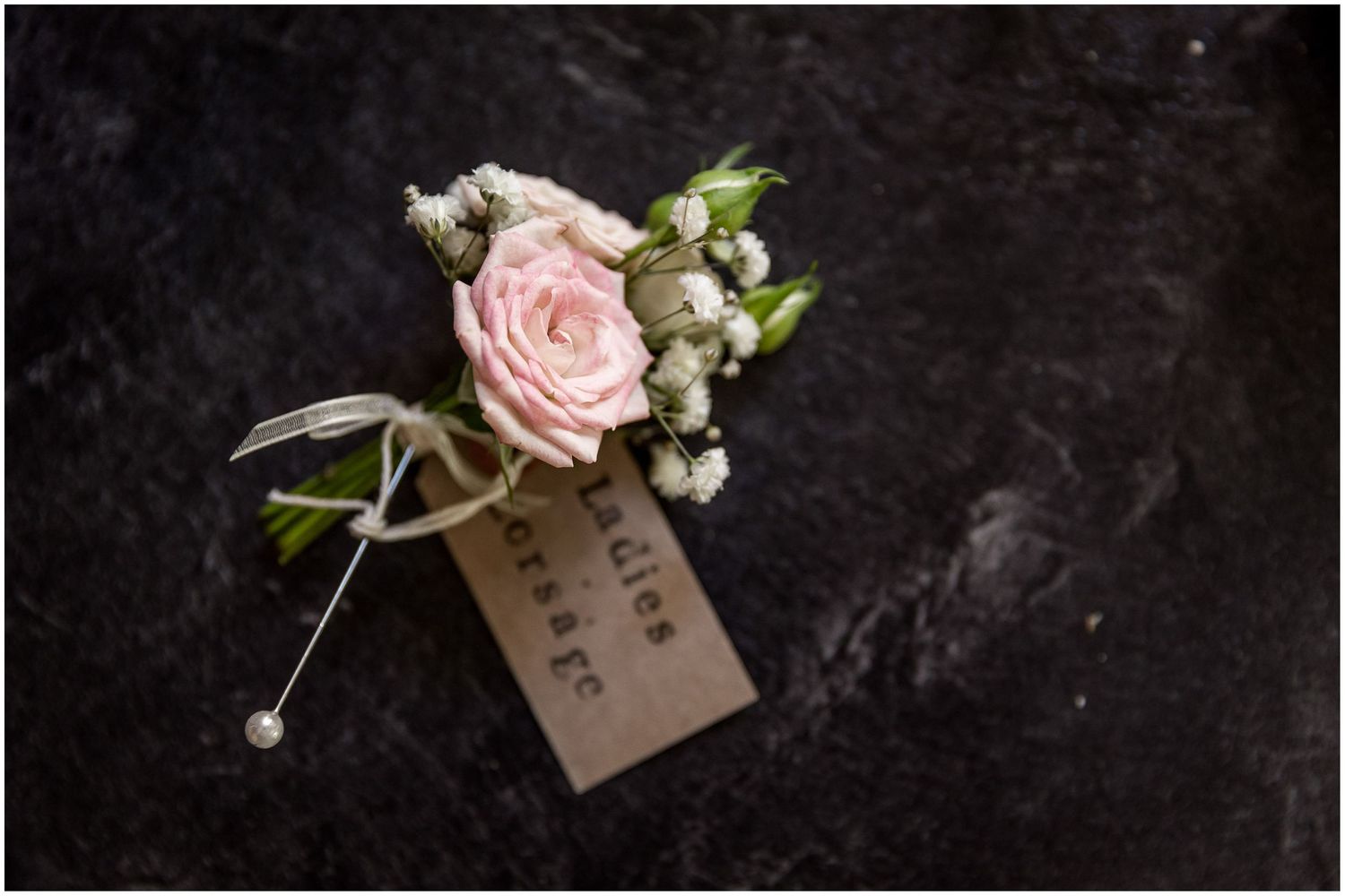 Delicate pink rose boutonnieres with name tags on dark background.