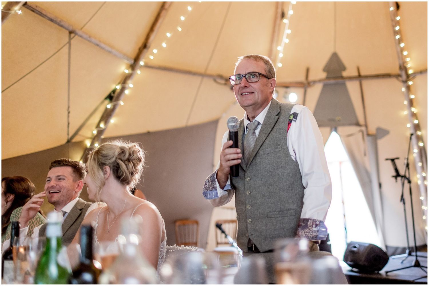 Wedding reception inside a tent decorated with string lights and elegant table settings.