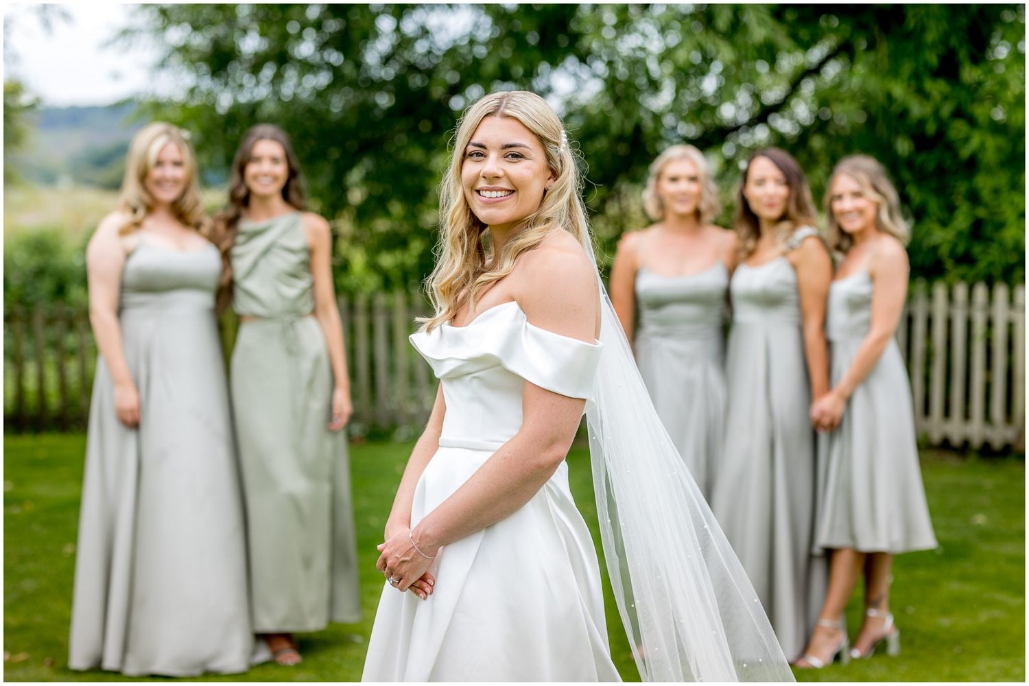 Bridesmaids in light gray dresses pose together outdoors during a summer wedding.