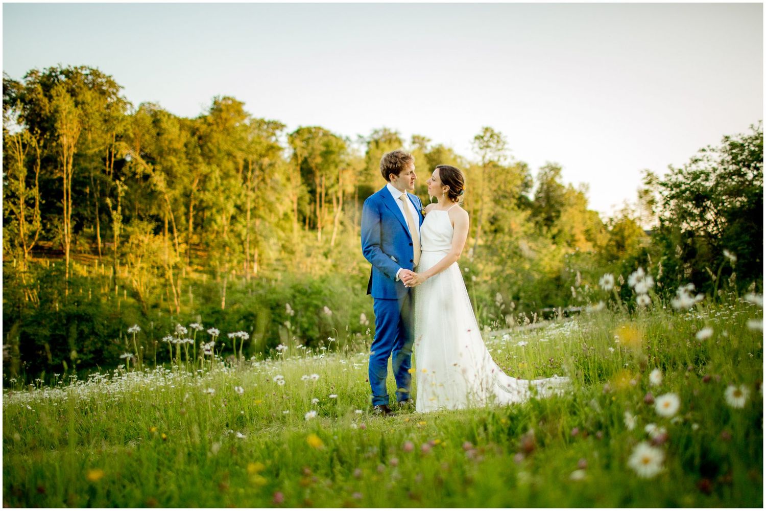 Wedding couple poses in a scenic field with wildflowers and natural summer lighting.