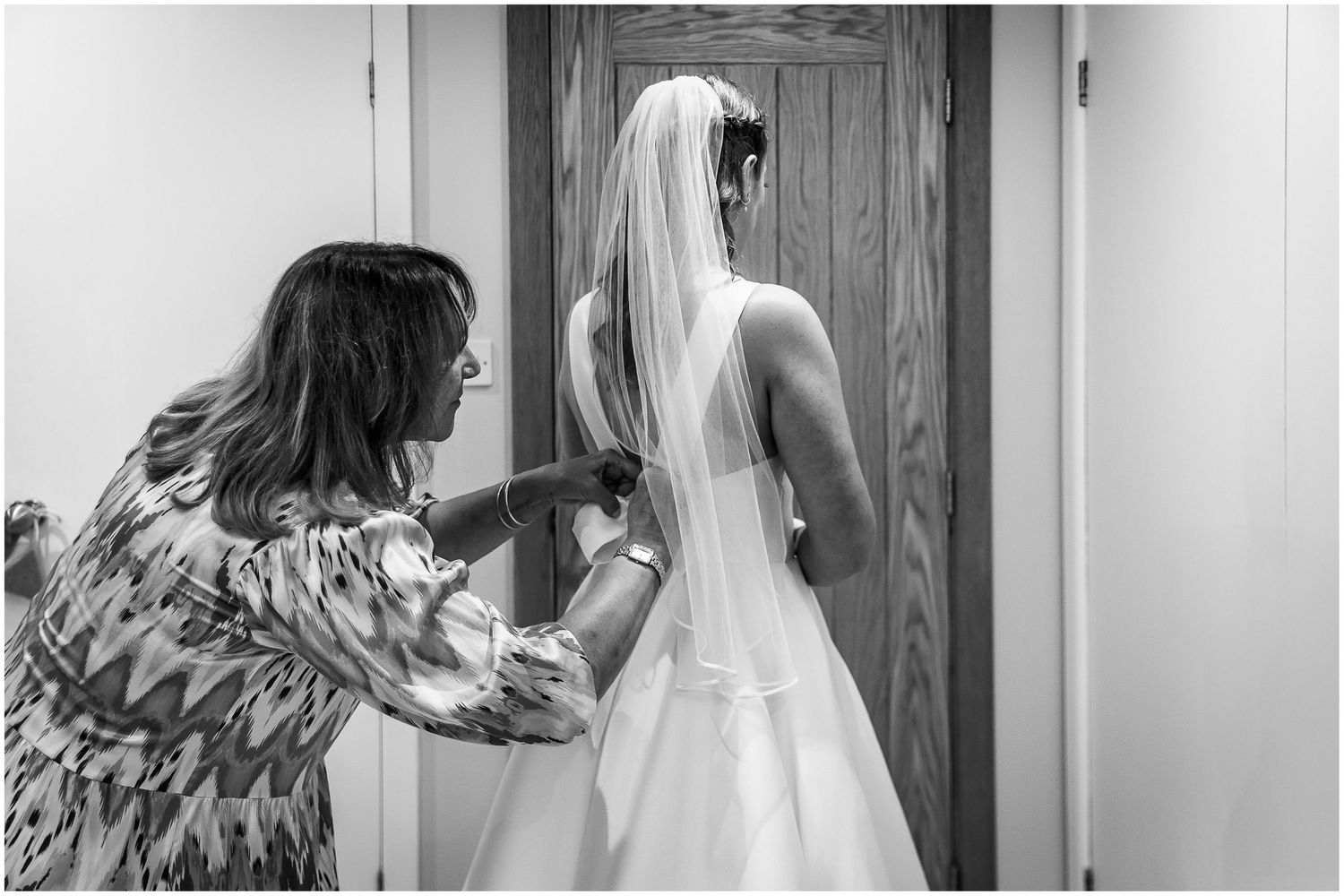 The bride's mother helps her daughter get into her wedding dress.